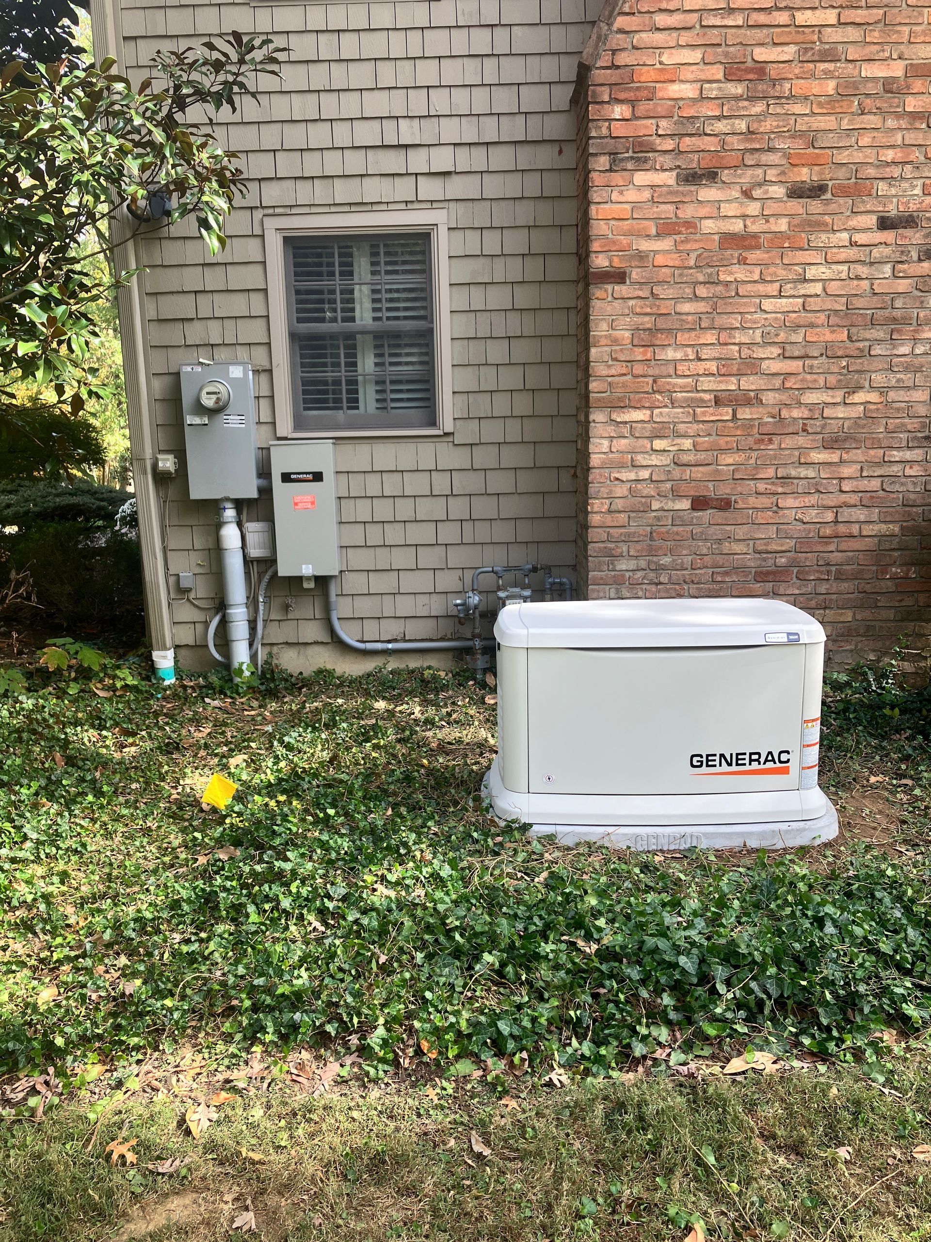 Outdoor air conditioning unit beside a brick house wall and utility meters in a grassy yard