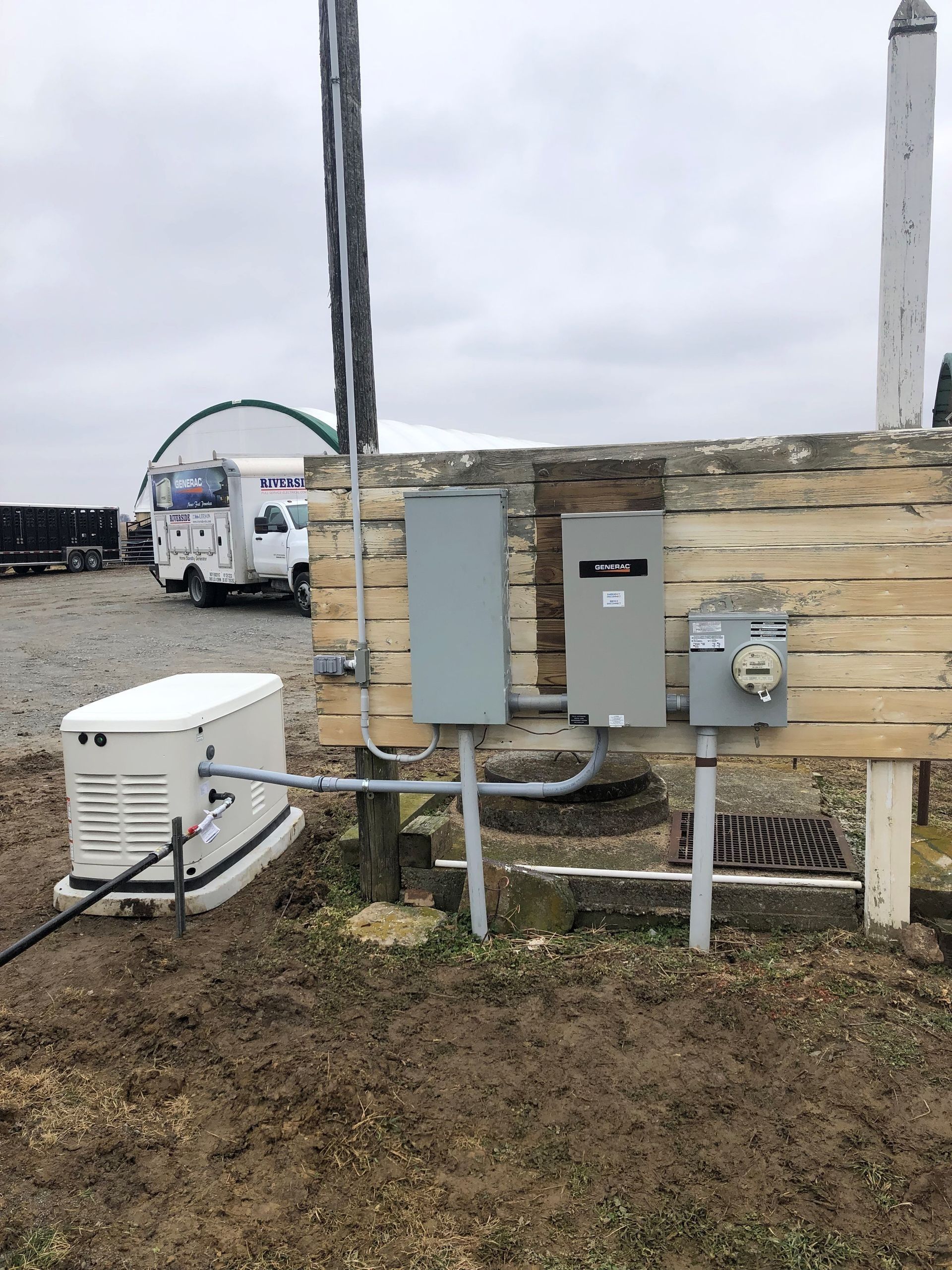 Utility boxes and pipes mounted on a wooden fence beside a cloudy parking lot.