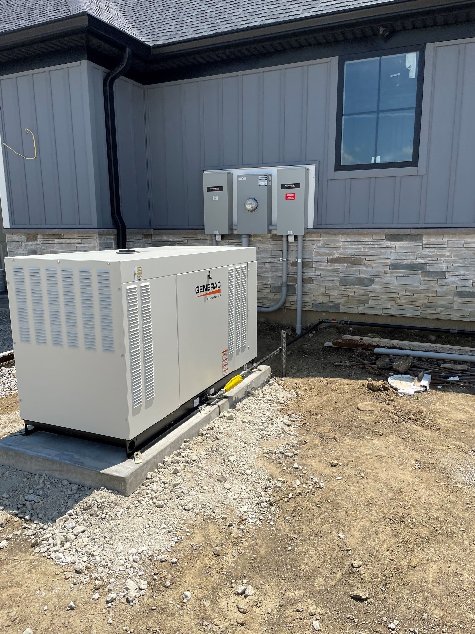 Outdoor HVAC unit beside a gray building with utility boxes and a stone base on gravel.