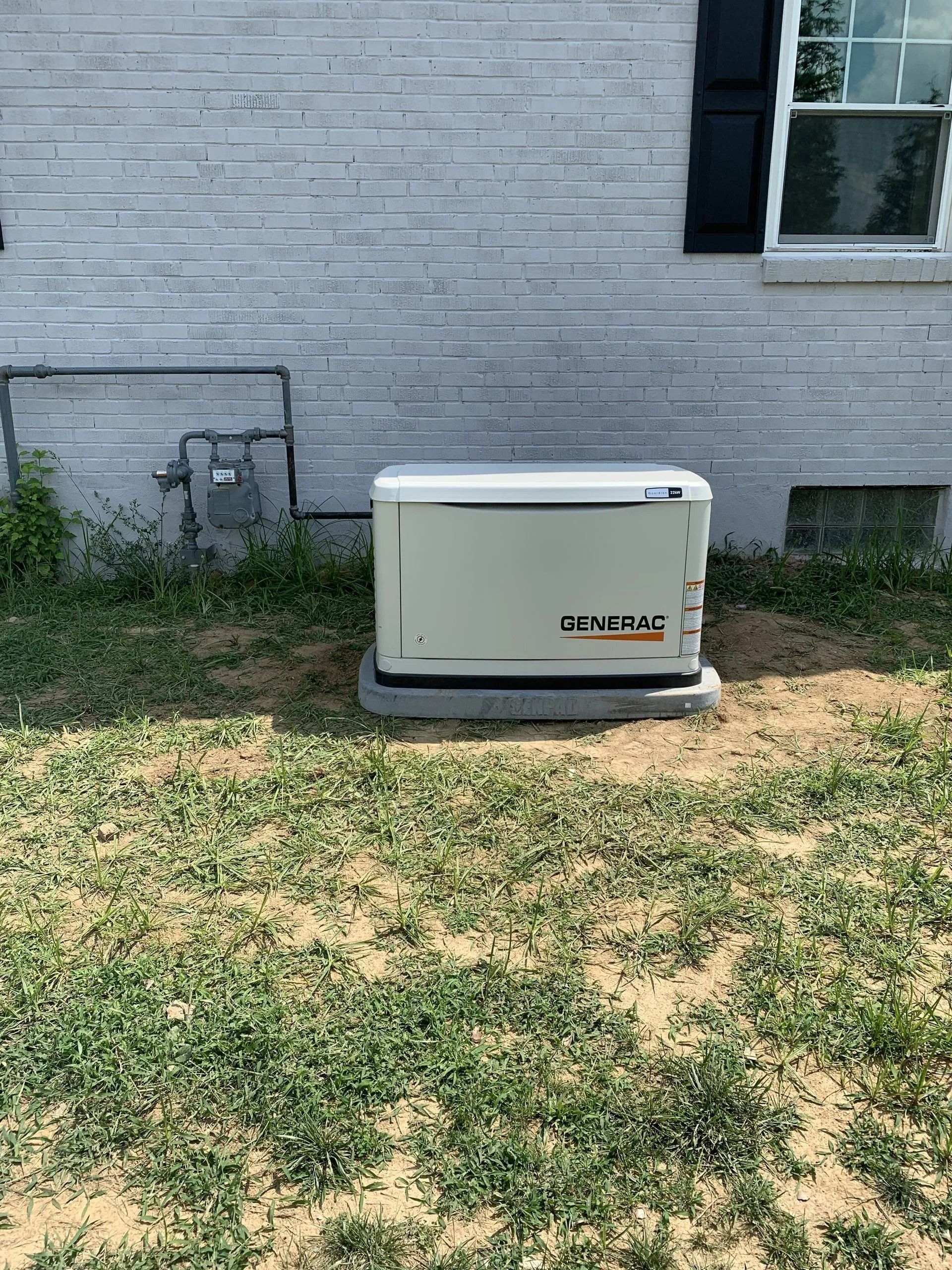 Outdoor AC unit beside a brick house wall on a patchy grass yard