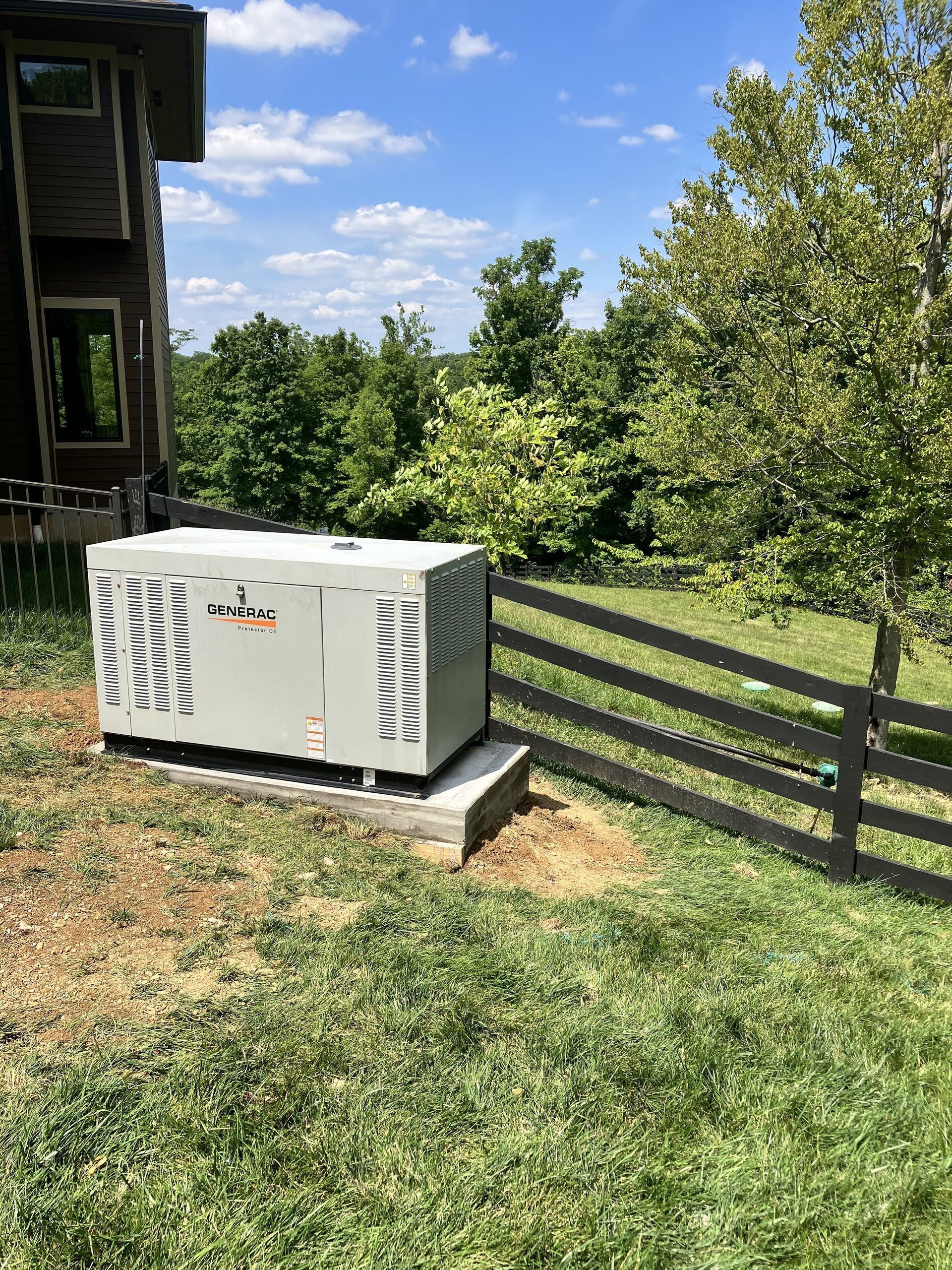 White utility box on a concrete pad beside a house and wooden fence in a sunny yard
