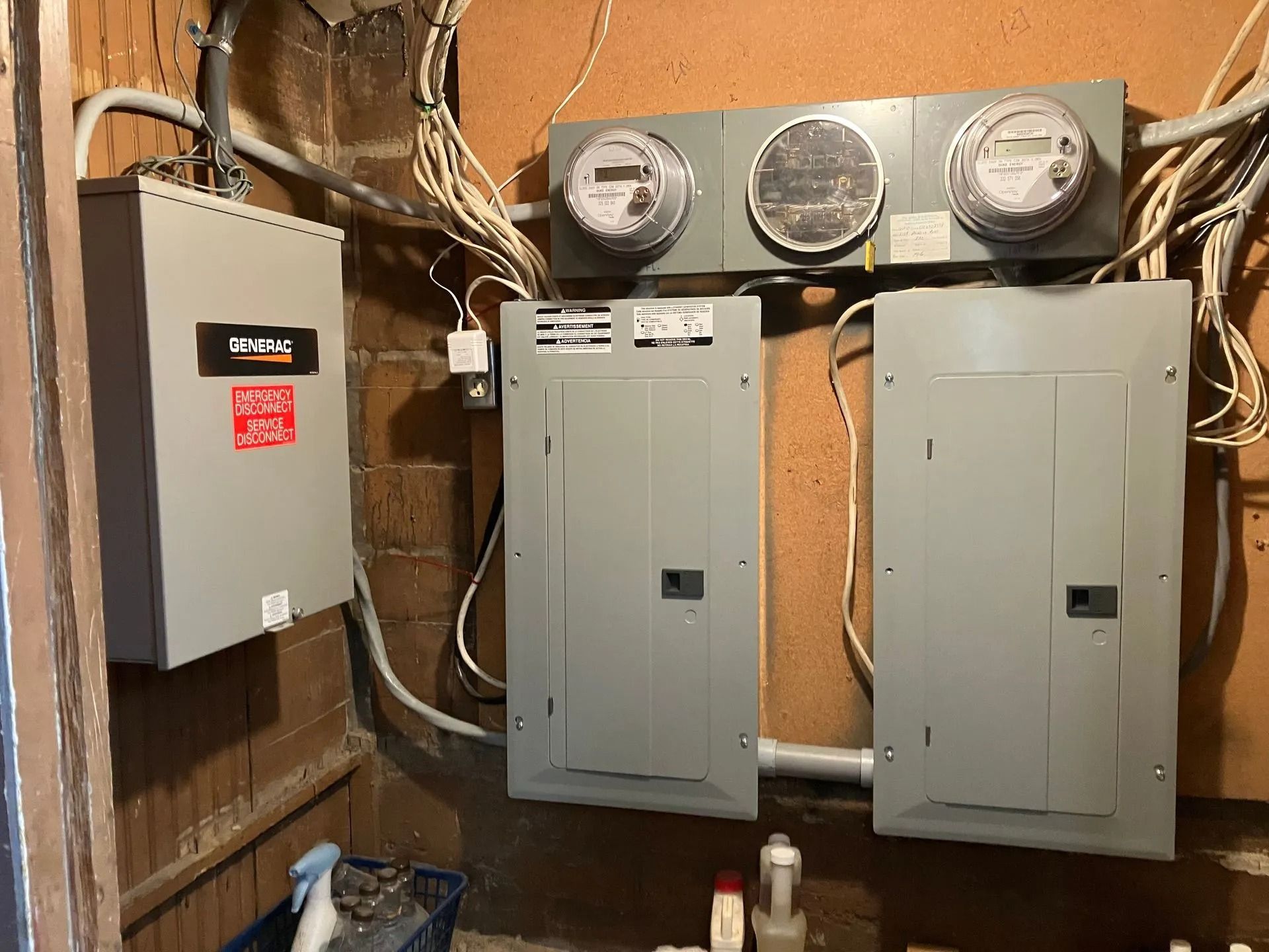 Wall-mounted electrical meters and gray breaker panels in an unfinished utility room