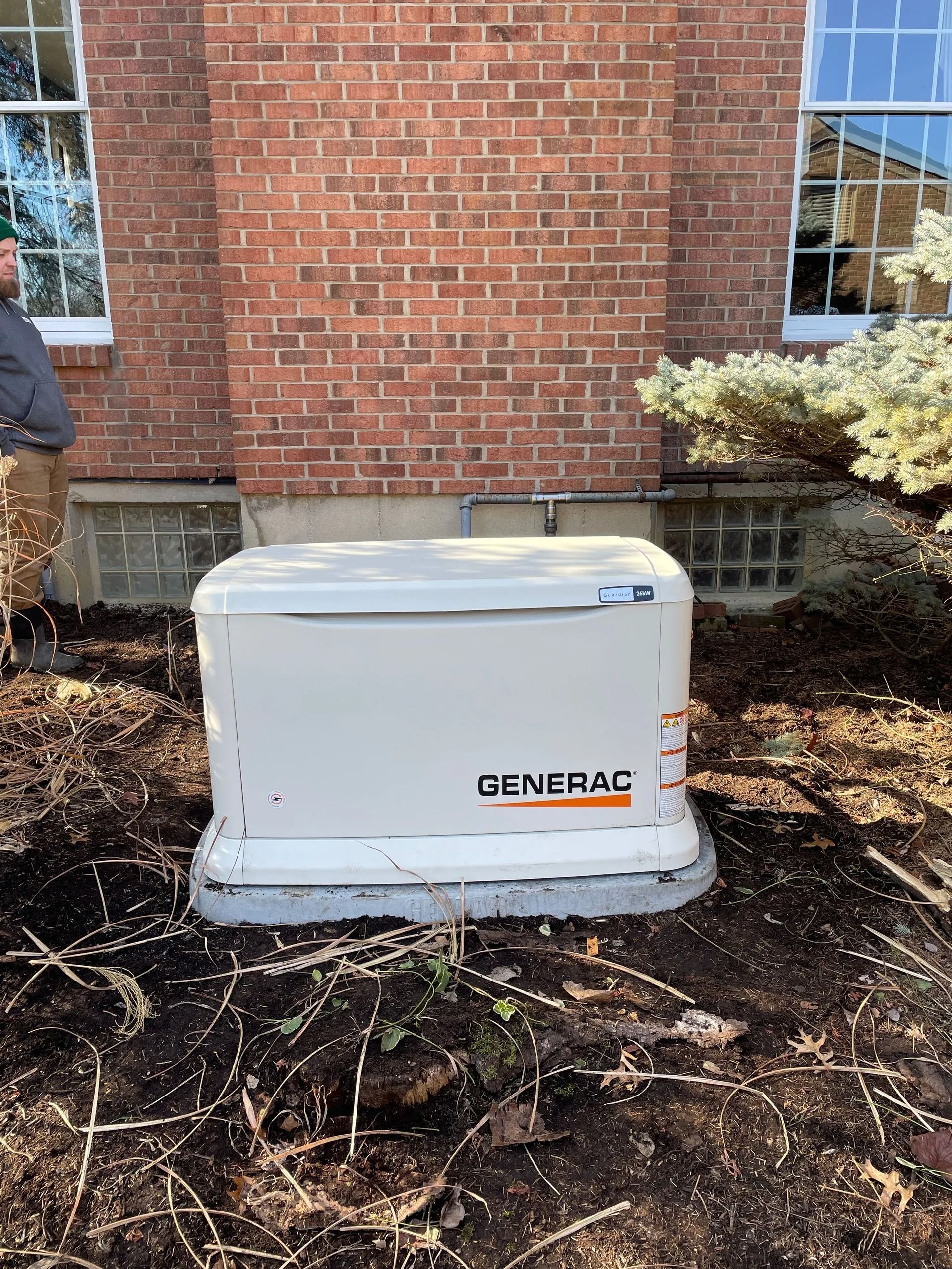 Generac home standby generator beside a brick house, surrounded by mulch and low shrubs