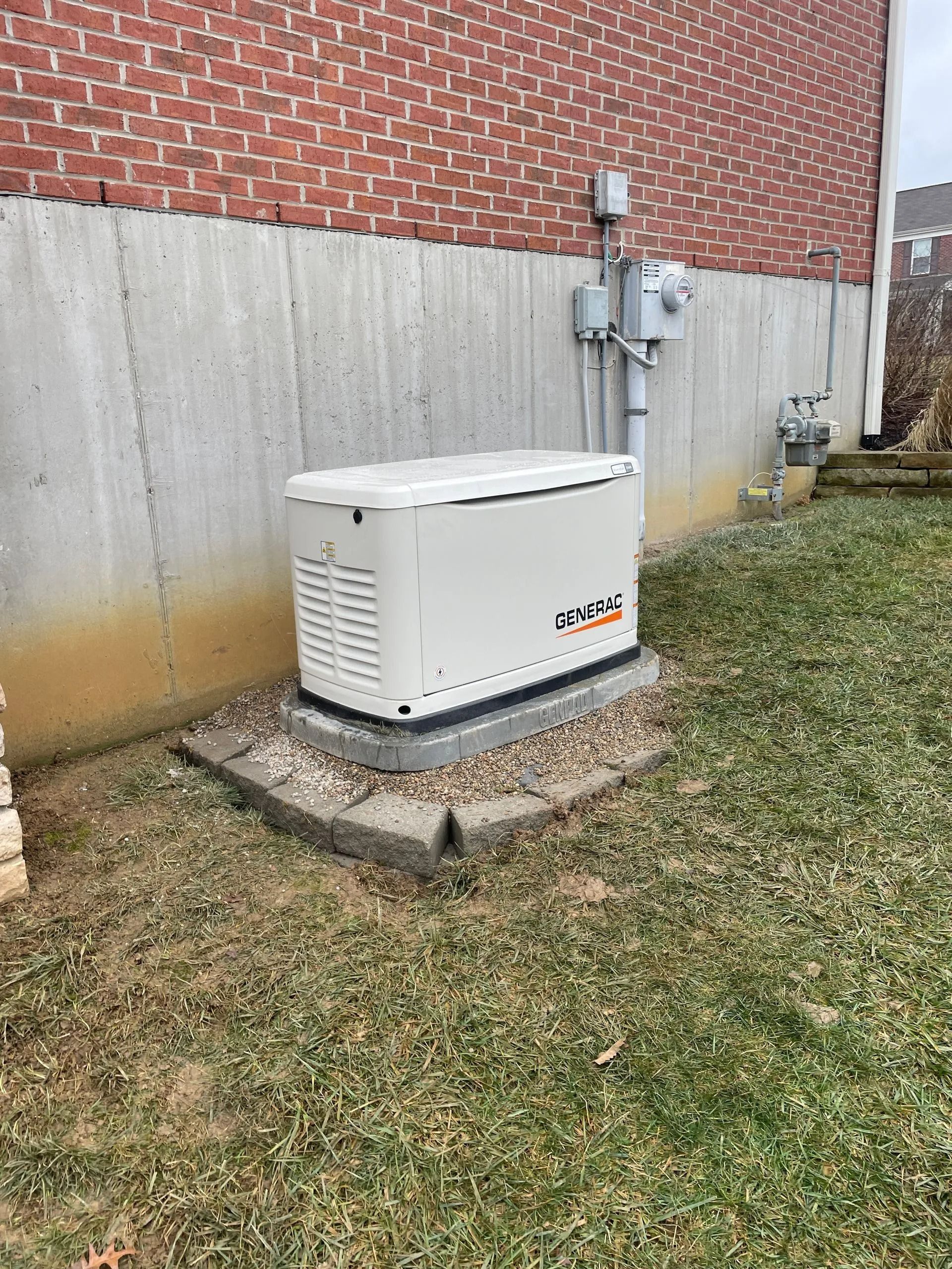 White generator beside a brick house on a concrete pad in a grassy yard