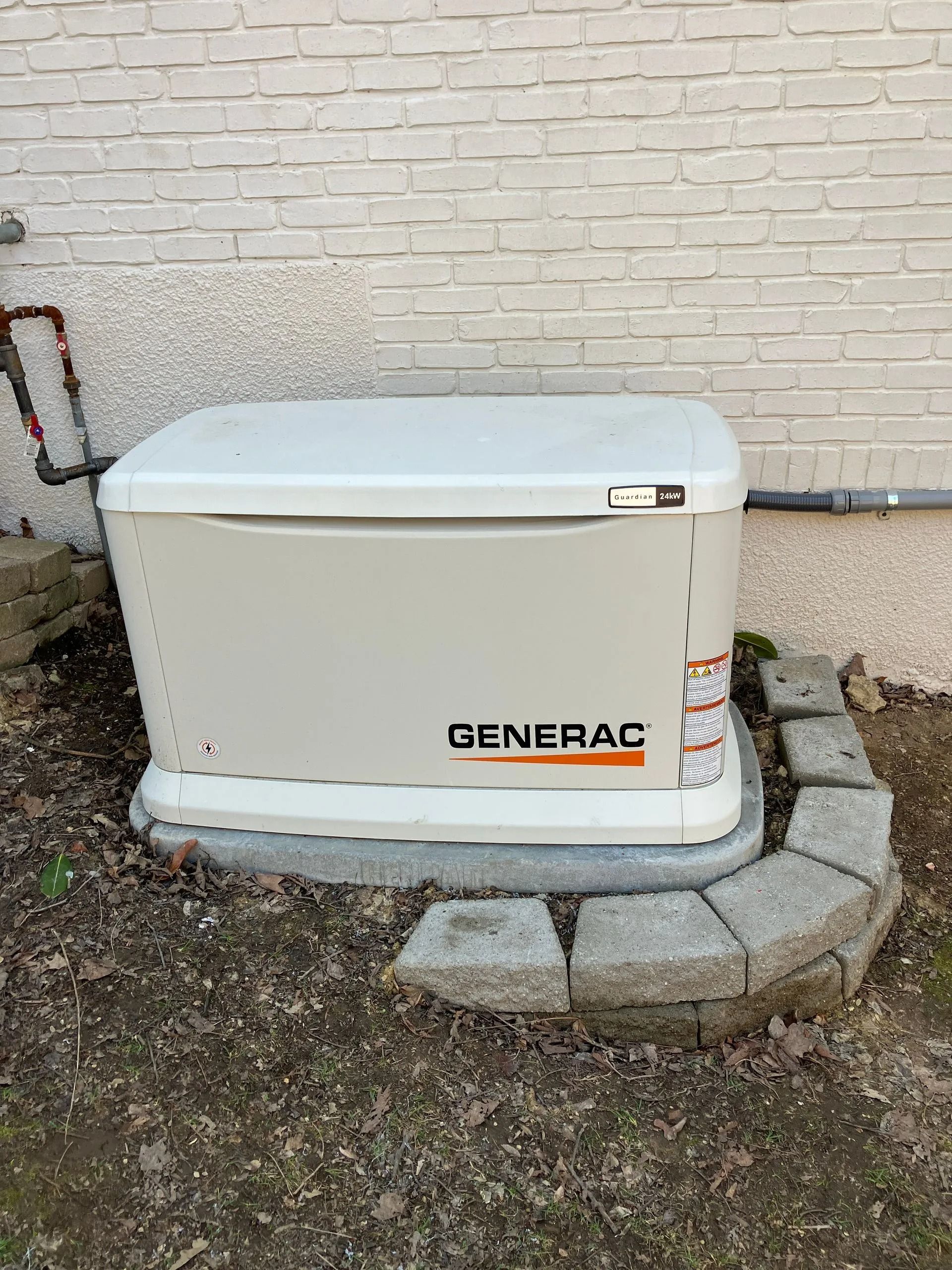 White Generac generator on a stone pad against a beige brick wall outdoors