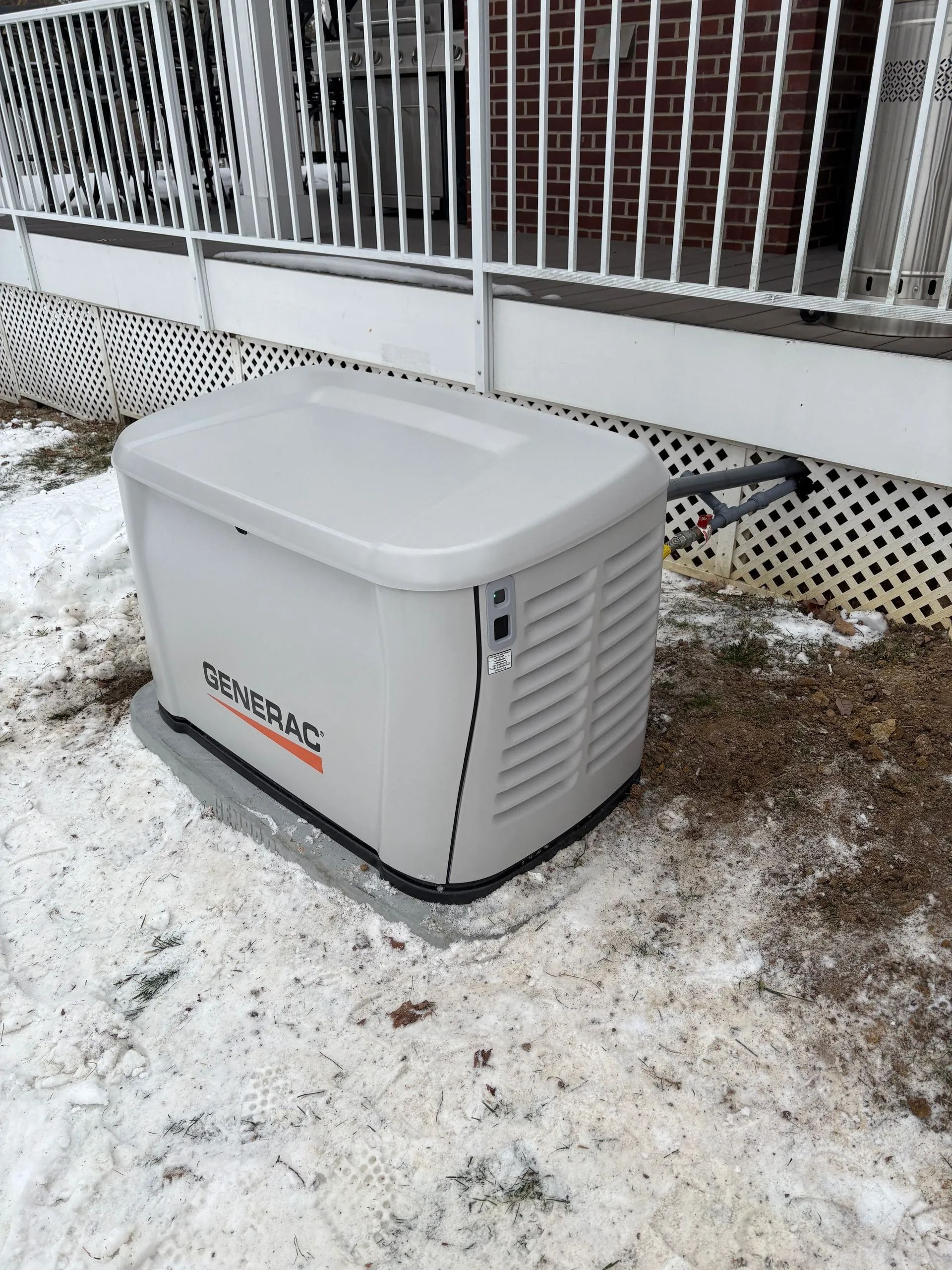 Portable generator on snow beside a house railing.