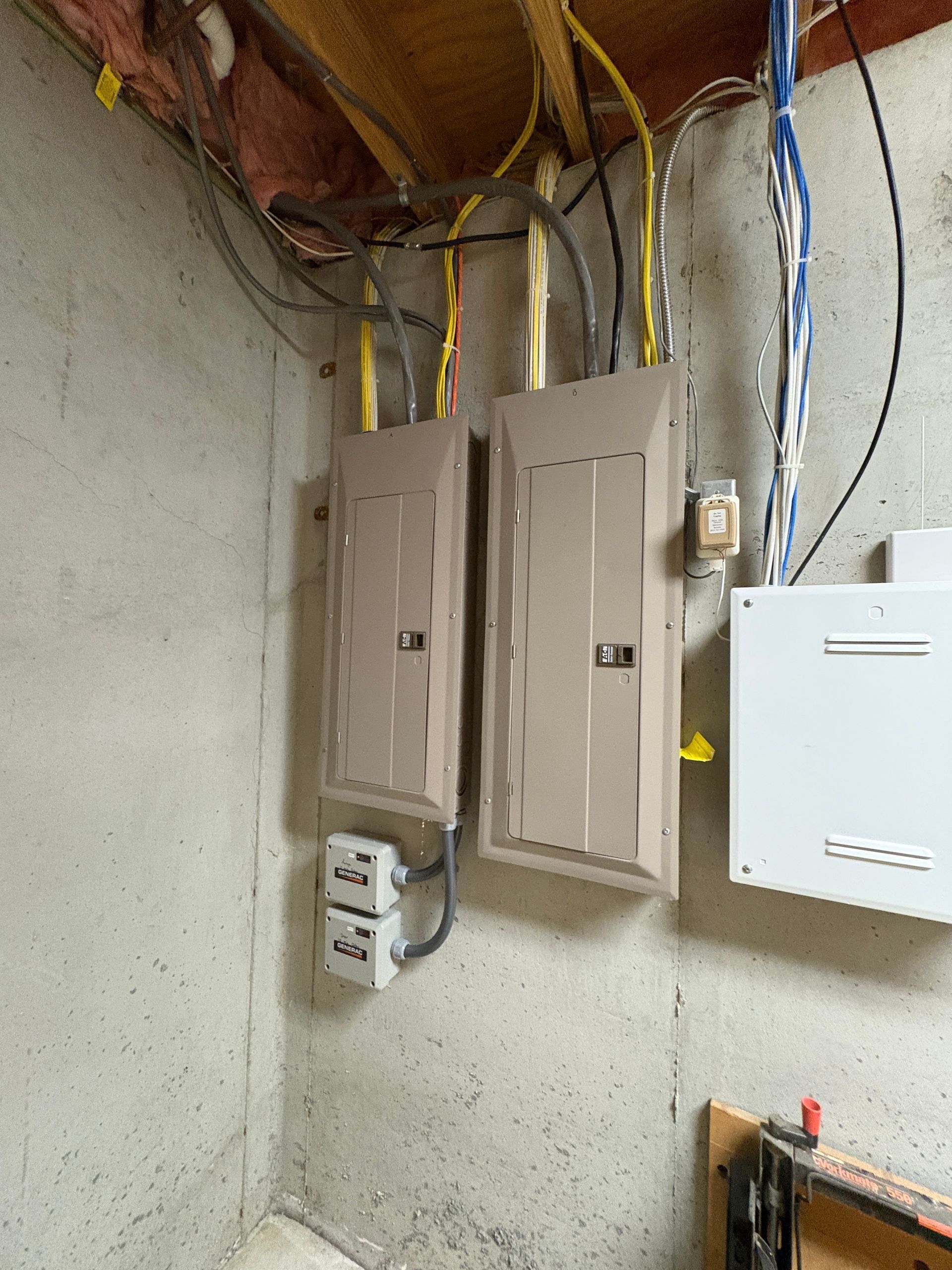 Utility meters and electrical panels mounted on a basement wall with exposed wiring overhead.