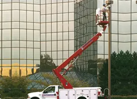 Utility worker in a red cherry picker repairing a tall netted structure outdoors.