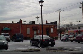 Snowy street with parked cars, a red brick building, and a lamppost under cloudy skies