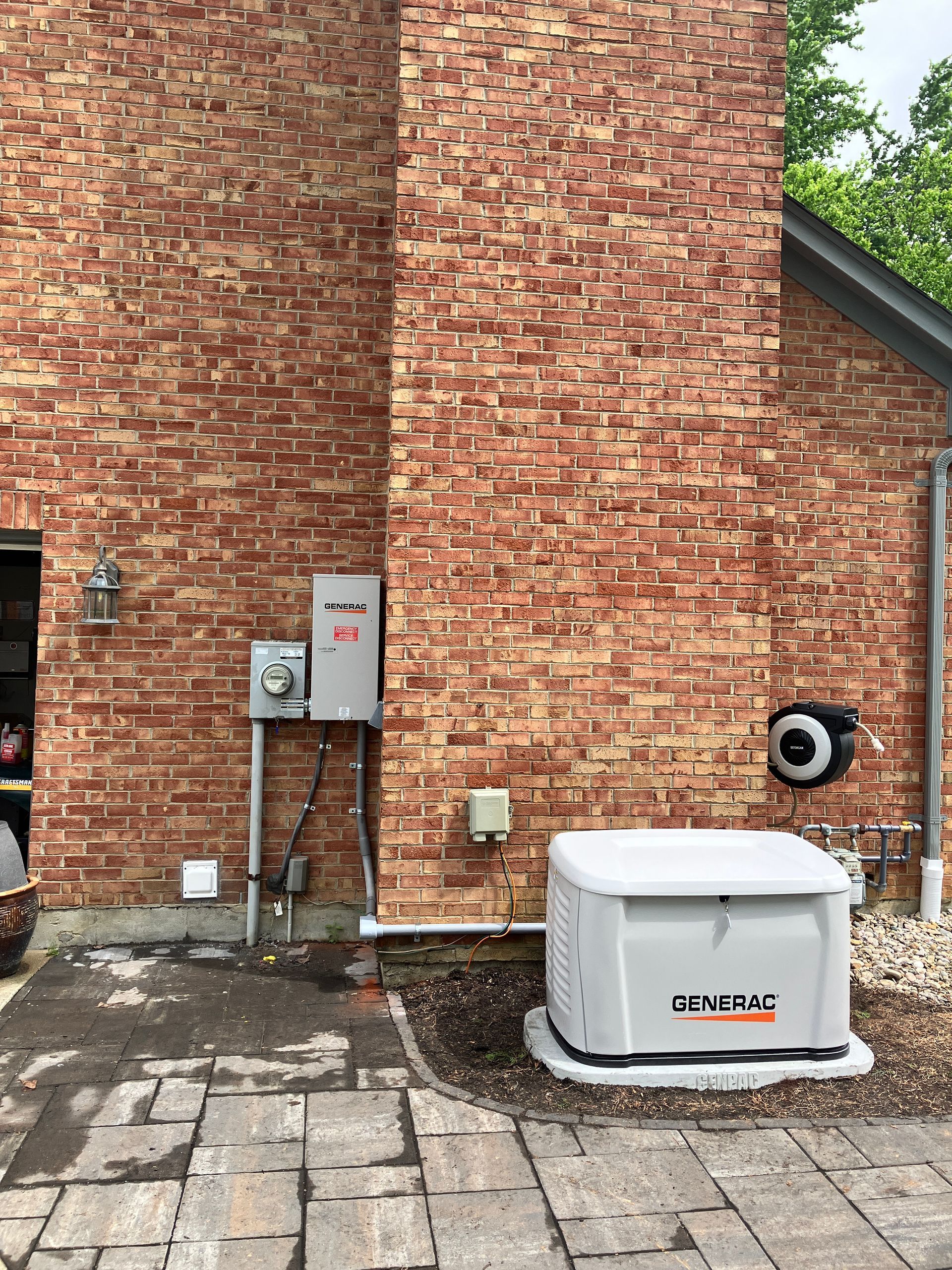 Brick building wall with electrical boxes and a gray generator on a paved patio.