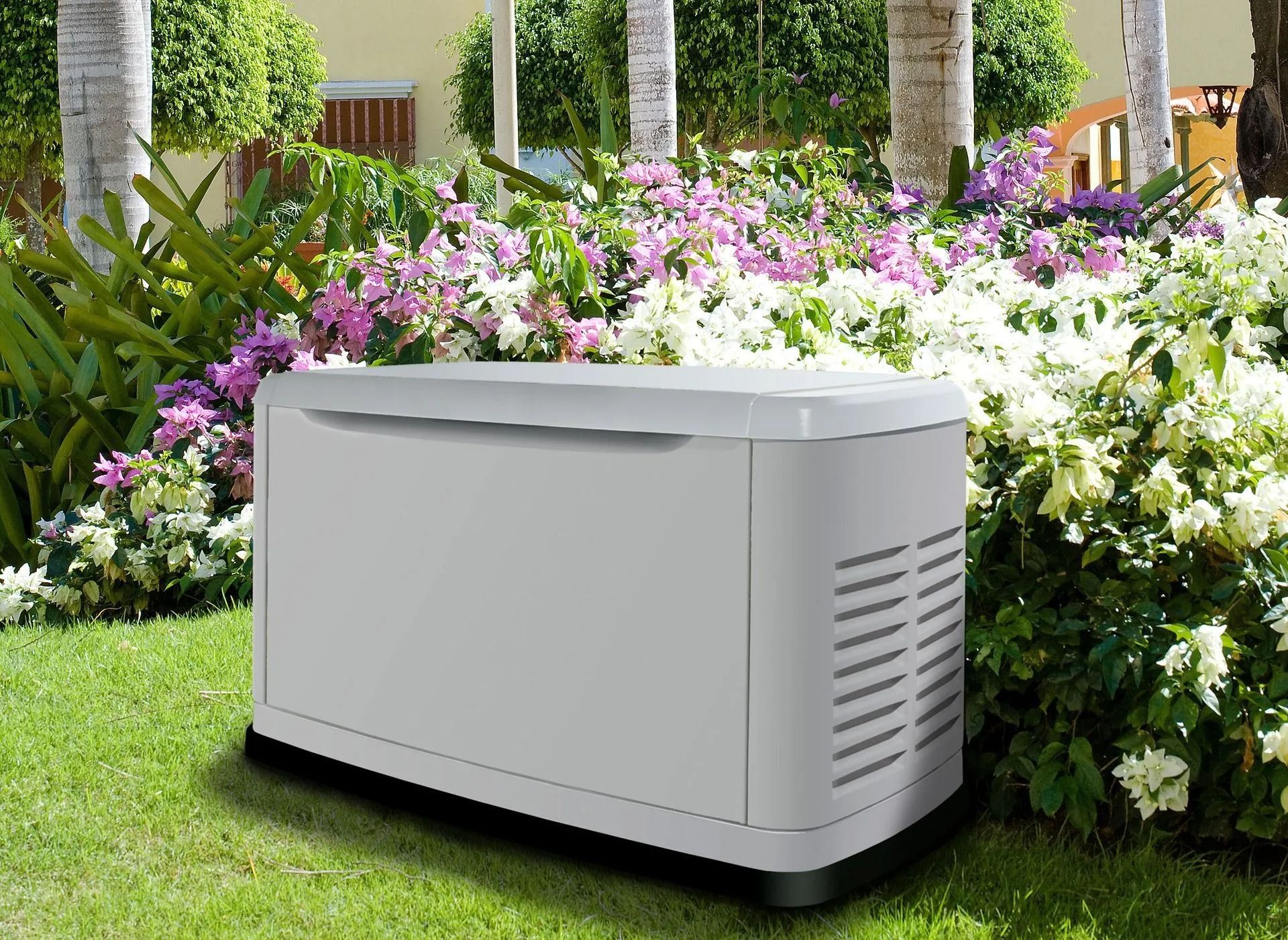 White outdoor generator beside colorful flowers in a garden