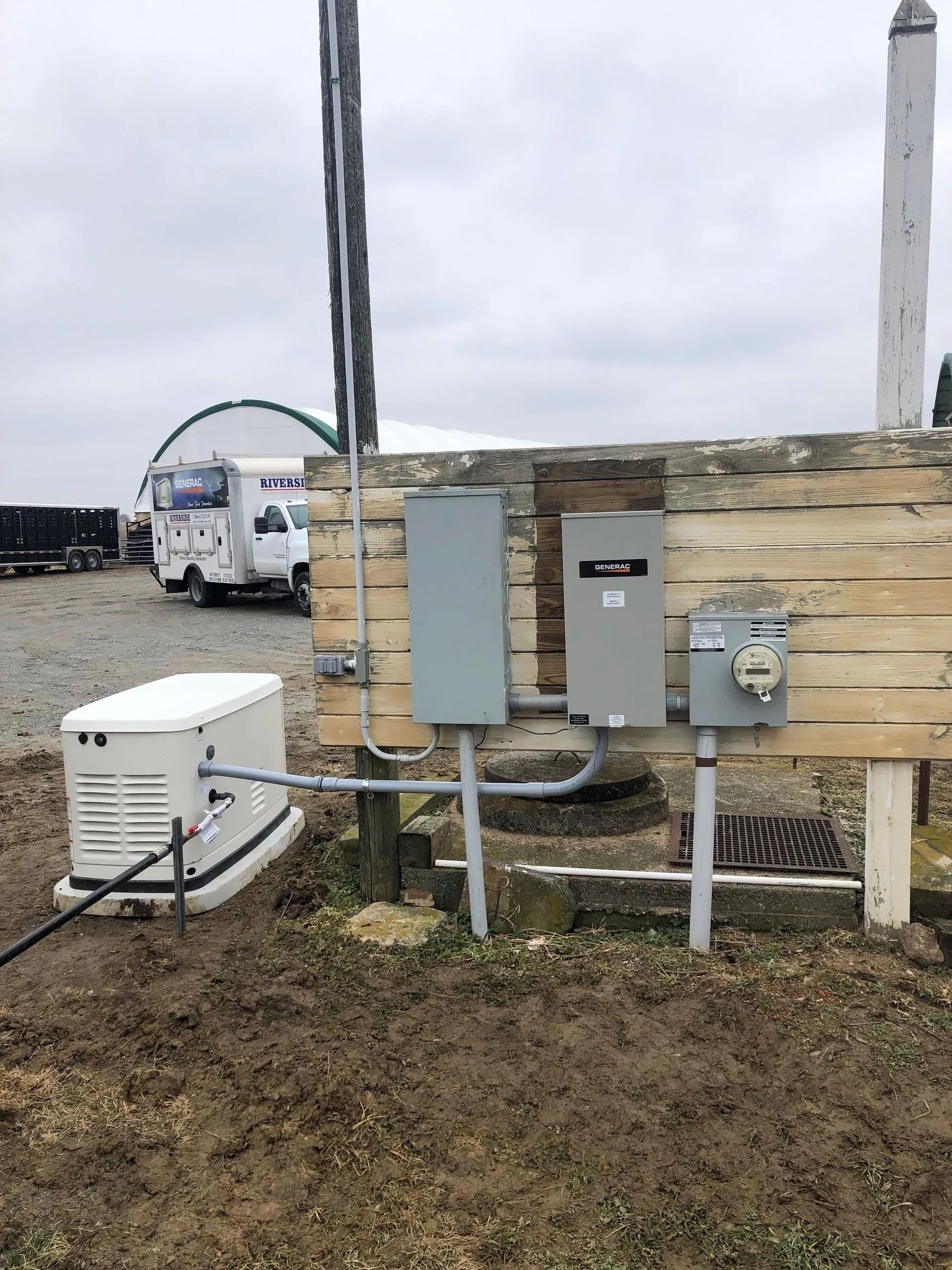 Utility boxes and conduit mounted on a weathered wooden wall outdoors, with a white equipment box nearby.
