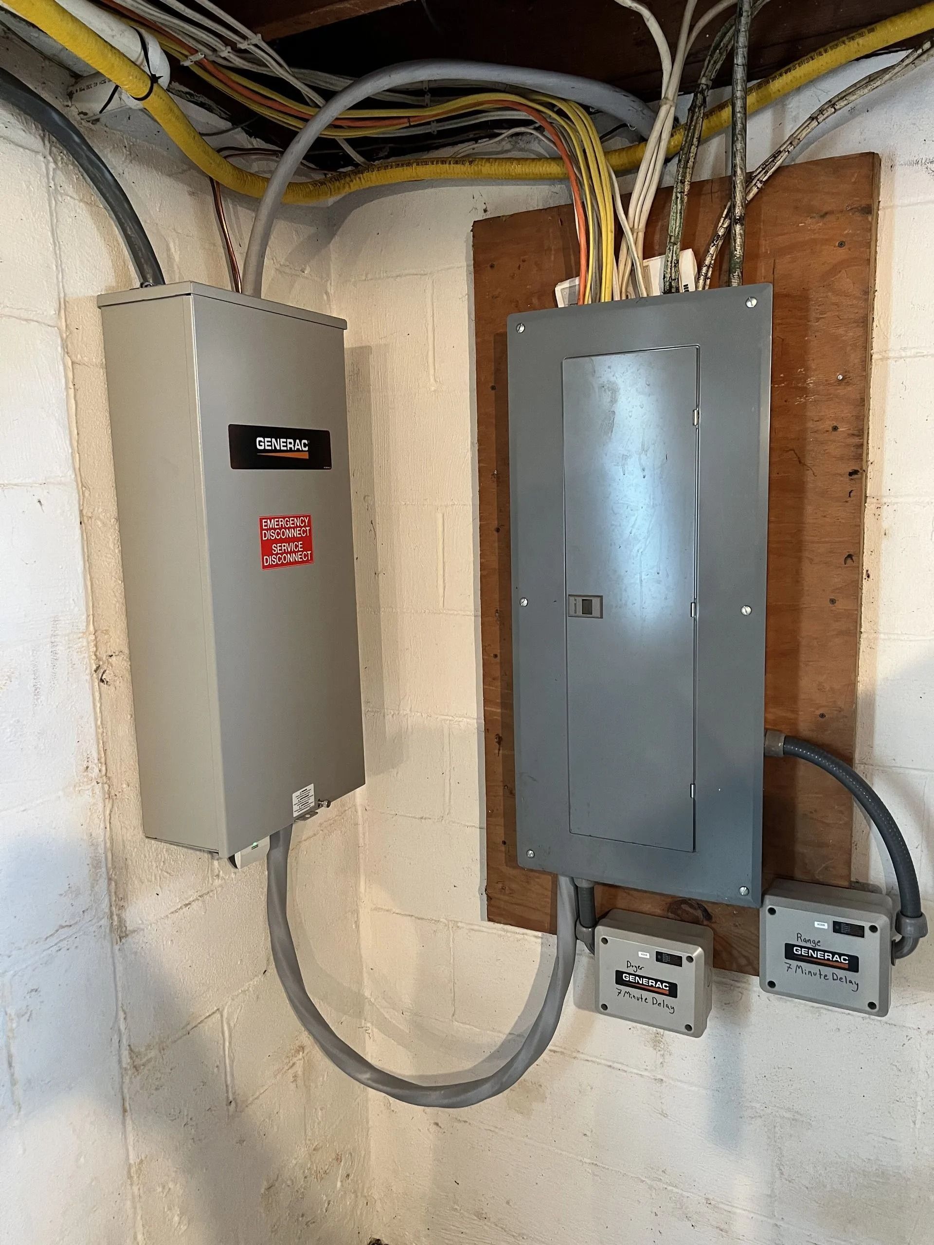 Two gray electrical panels with exposed wiring mounted on a basement wall