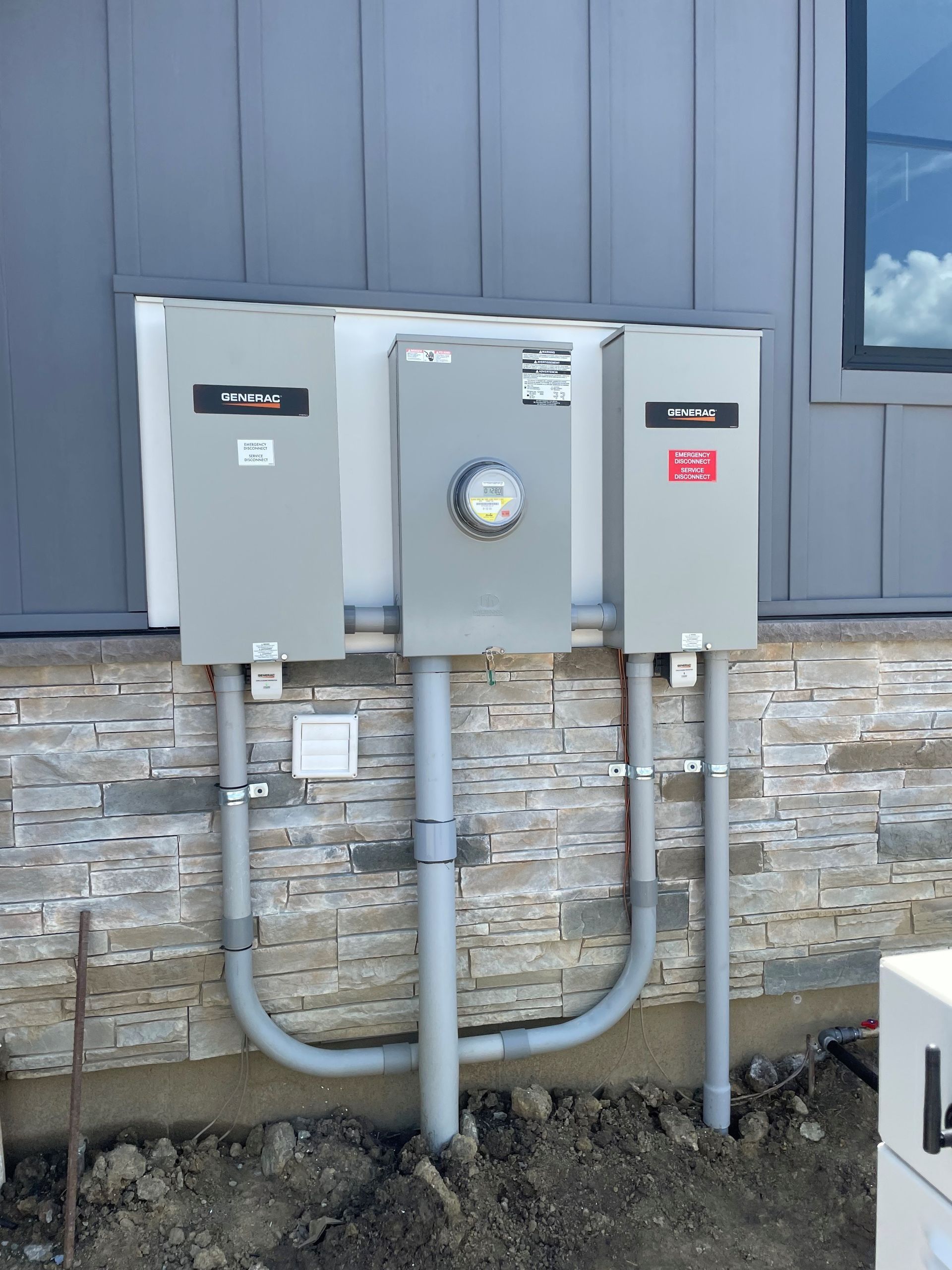 Three gray utility boxes mounted on a stone wall with conduit pipes below