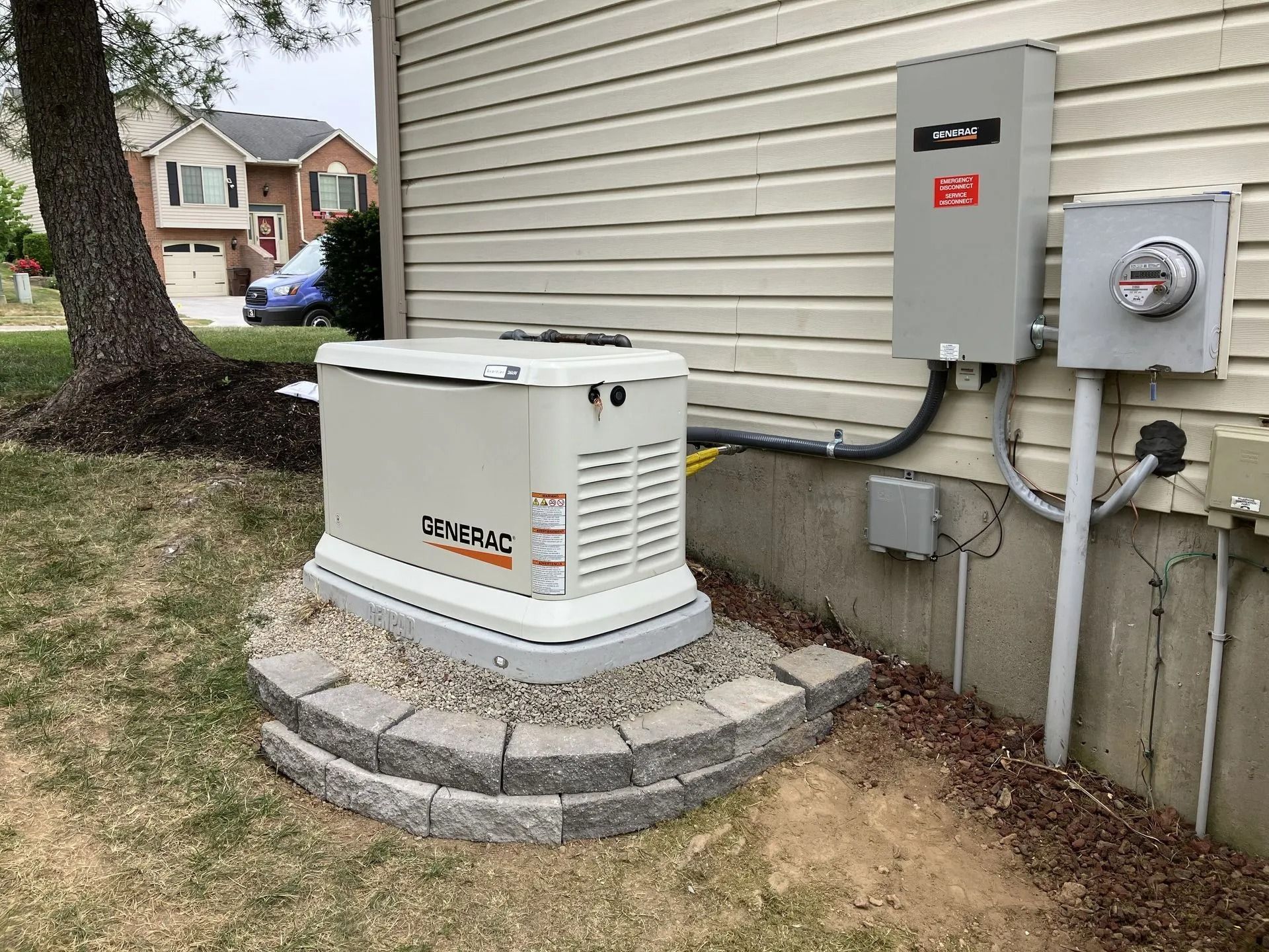 Outdoor generator beside a house, mounted on a stone base near utility meters.