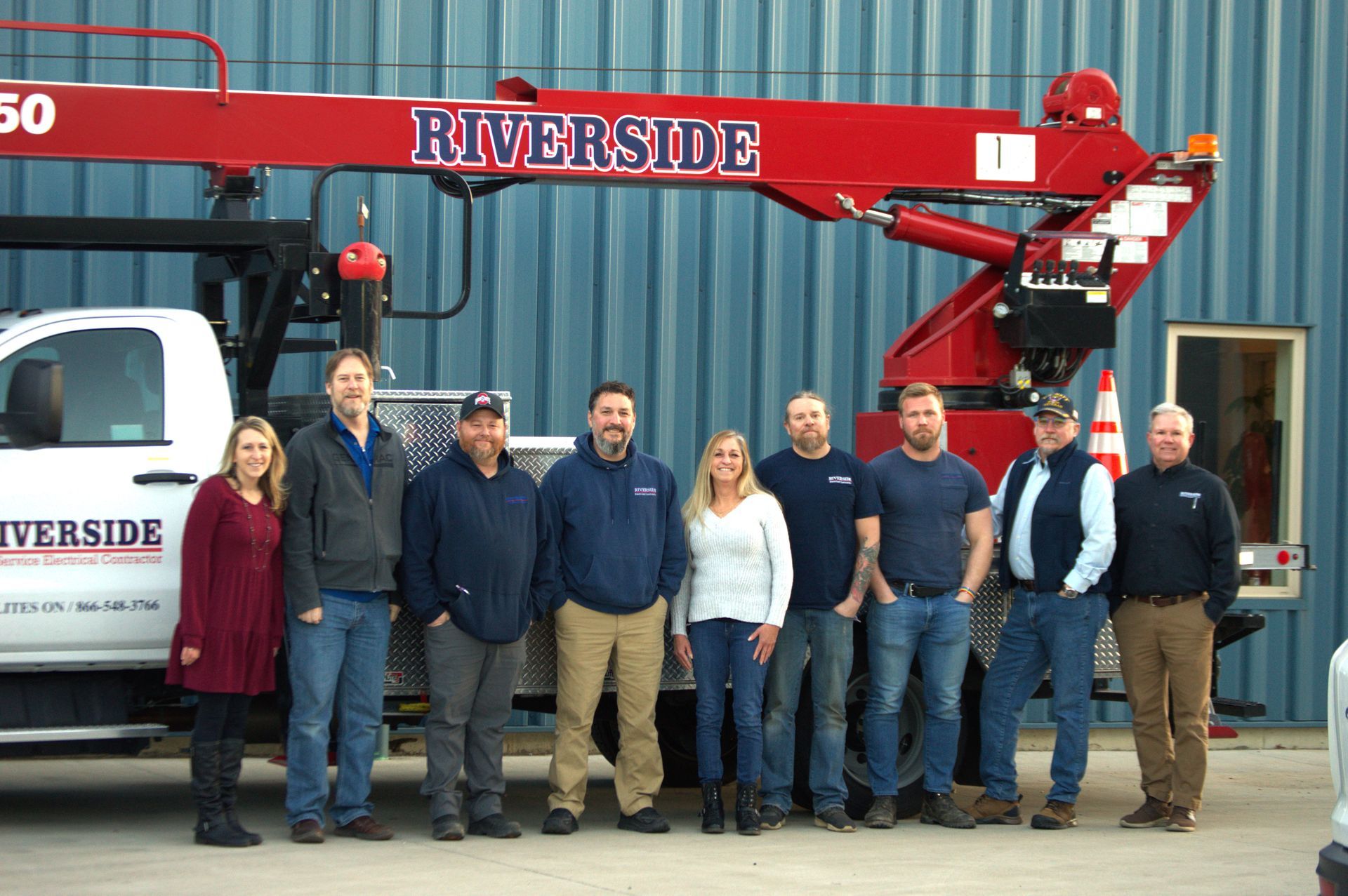Nine people standing in front of a red Riverside truck crane and blue shipping container