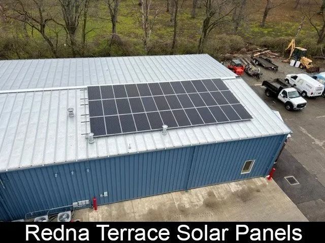 Solar panels on a blue building roof, with trees and parked vehicles nearby.