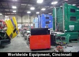 Industrial warehouse with colorful heavy equipment and machinery lined up indoors, labeled “Worldwide Equipment, Cincinnati”