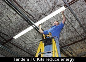 Worker installing a long fluorescent light on a ceiling using a yellow ladder; caption reads “Tandem T8 Kits reduce energy”