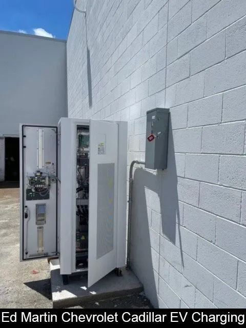 Open EV charging cabinet beside a white cinderblock wall in a parking lot