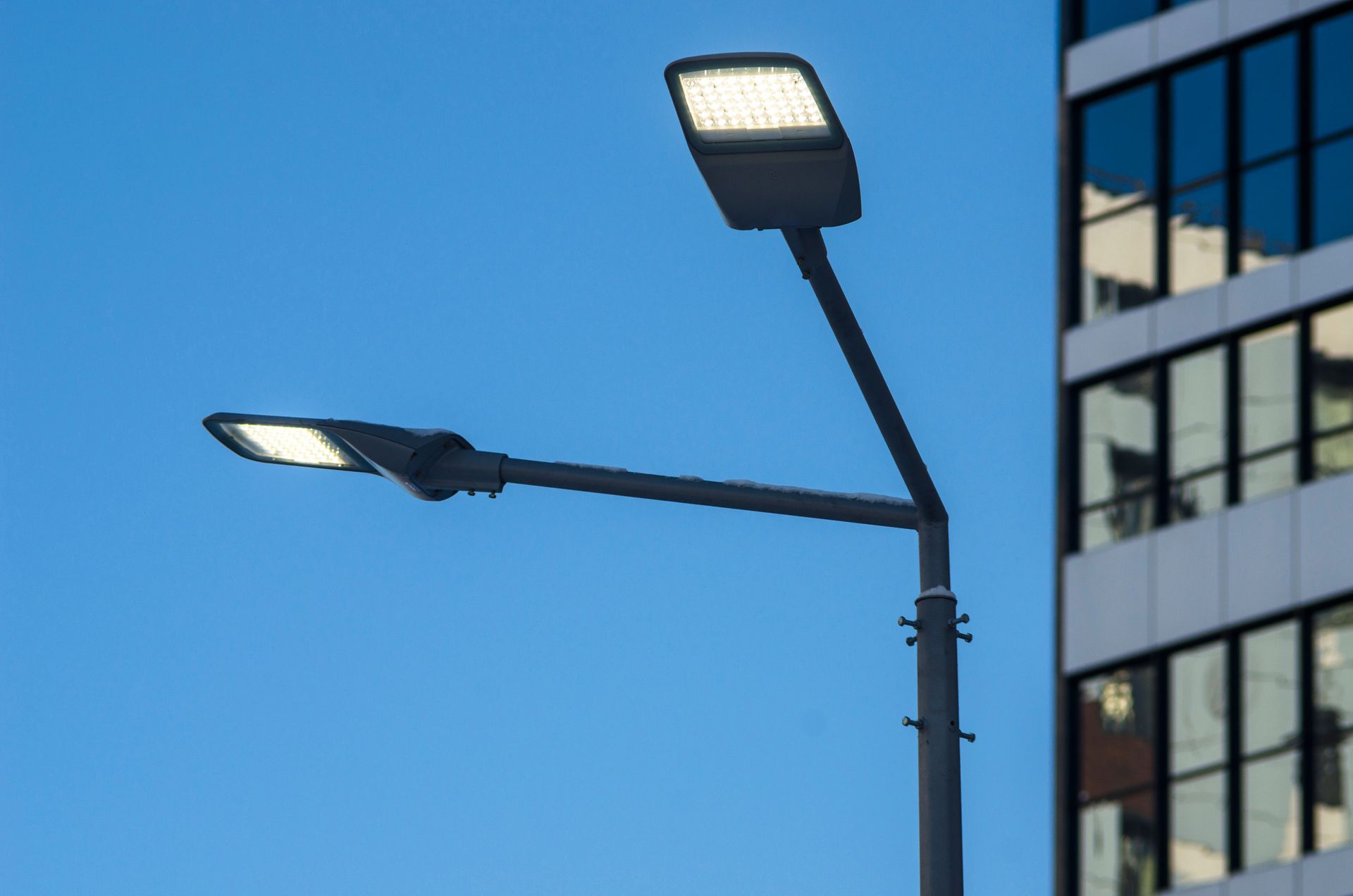 Two streetlights against a blue sky beside a modern building