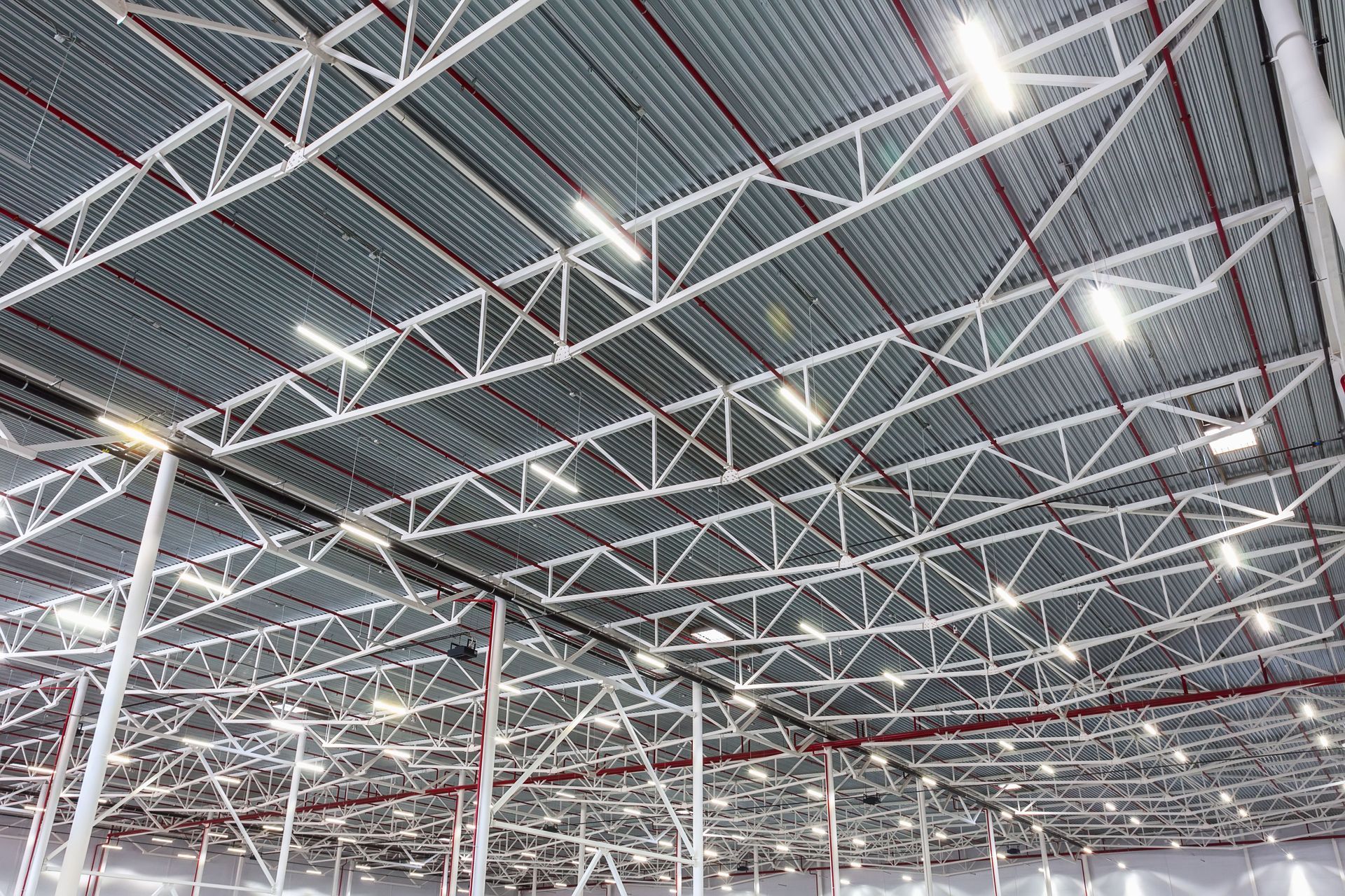 Interior of a large industrial warehouse with a white steel truss ceiling and bright overhead lights