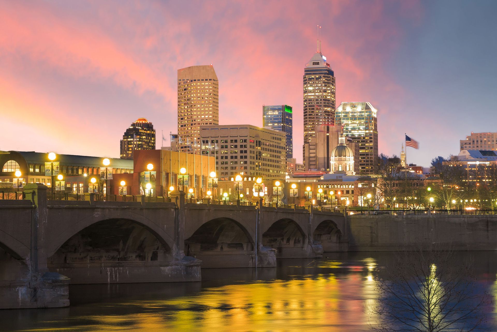 City skyline at sunset with a bridge in the foreground and pink clouds over the water.