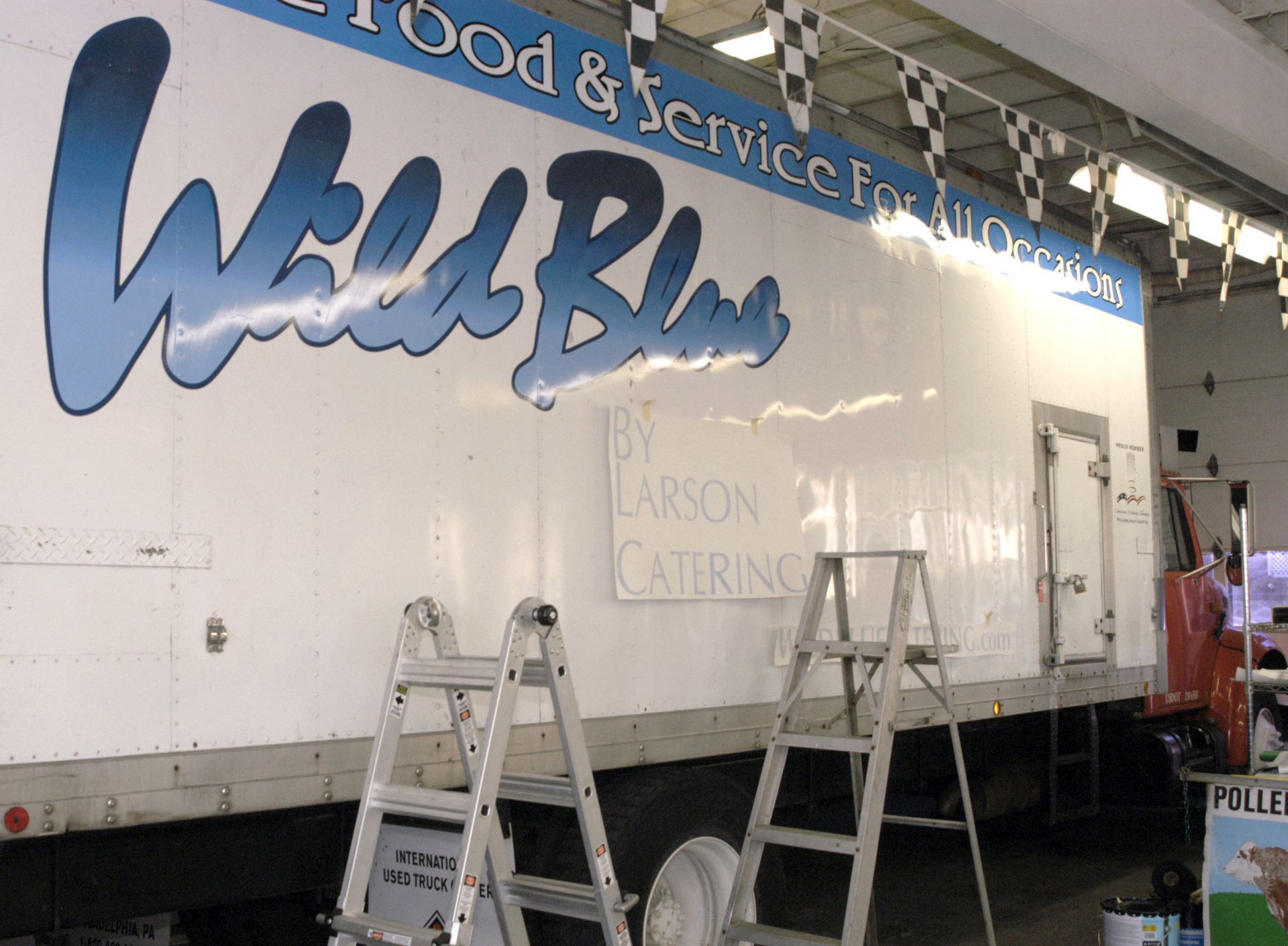 White food service trailer with blue “Wells Blue” logo and two ladders in front