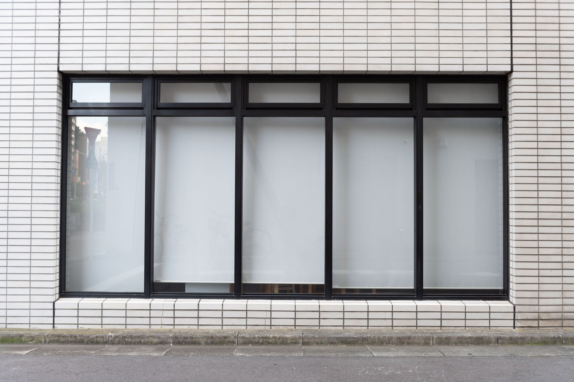 Closed black-framed window in a white tiled wall, with frosted glass panels.
