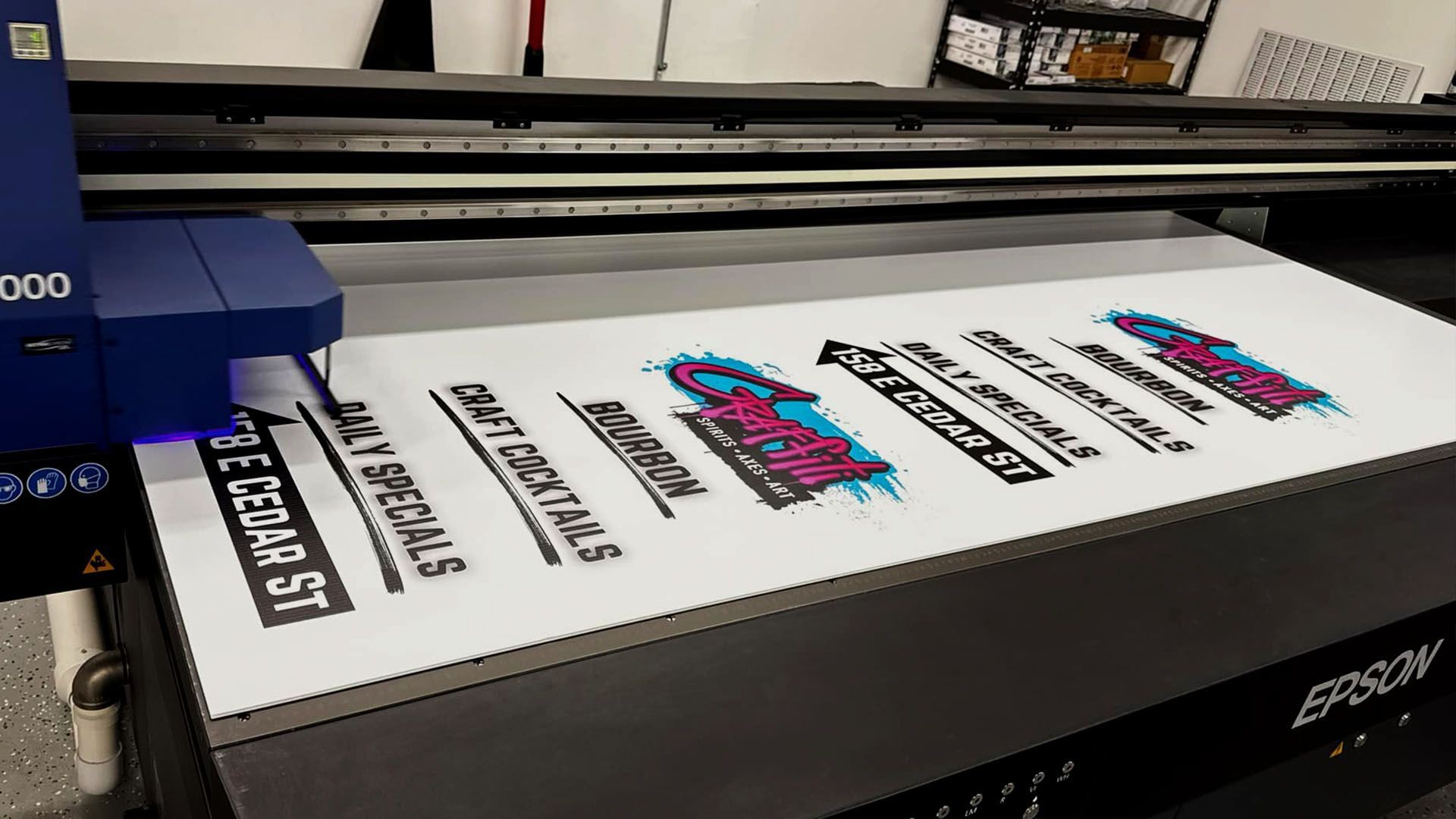 Large-format printer printing colorful logo decals on white material in a workshop