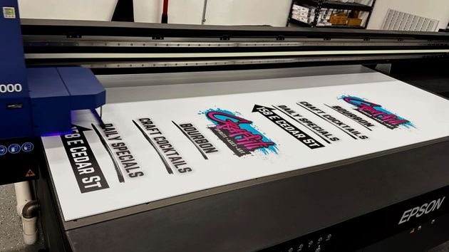Large-format printer printing colorful logo decals on white material in a workshop