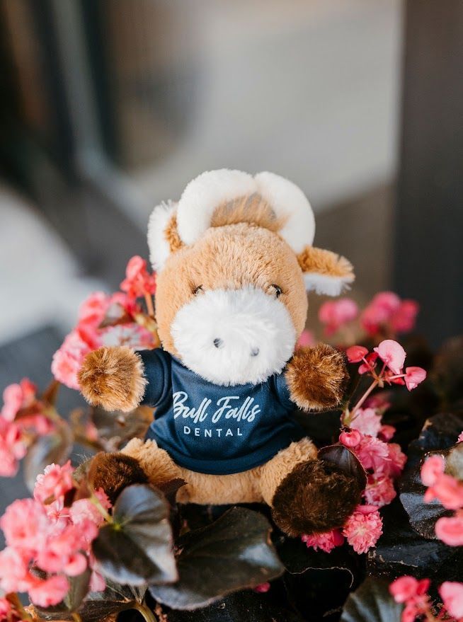 A stuffed cow wearing a blue shirt is sitting on top of flowers.