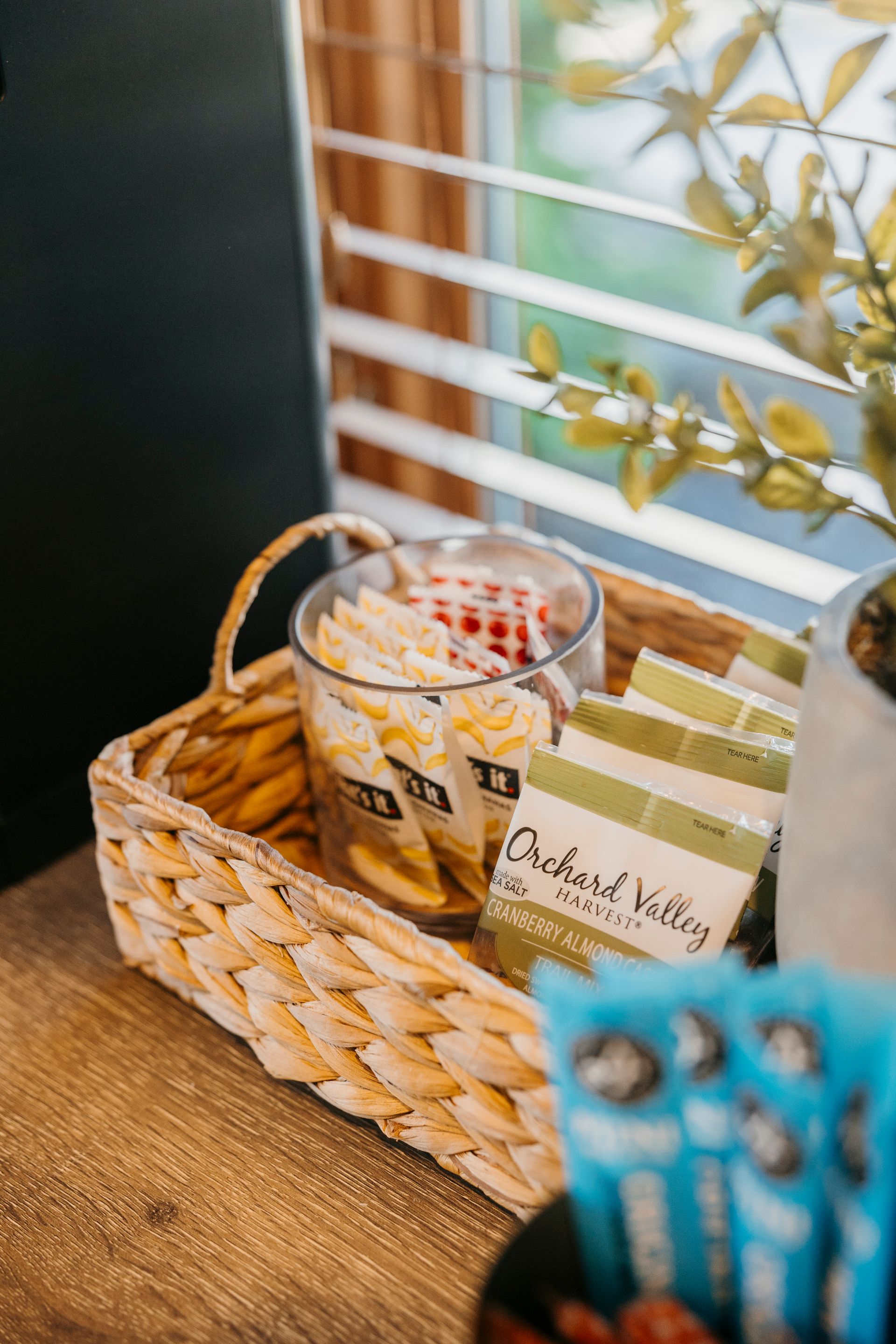 A basket filled with snacks is sitting on a wooden table next to a window.
