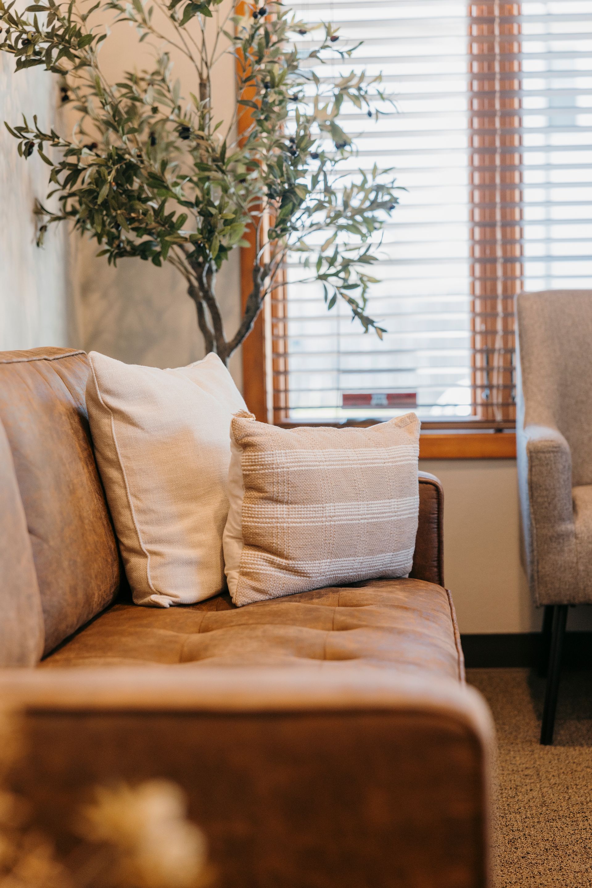 A brown couch with white pillows is sitting in a living room next to a window.