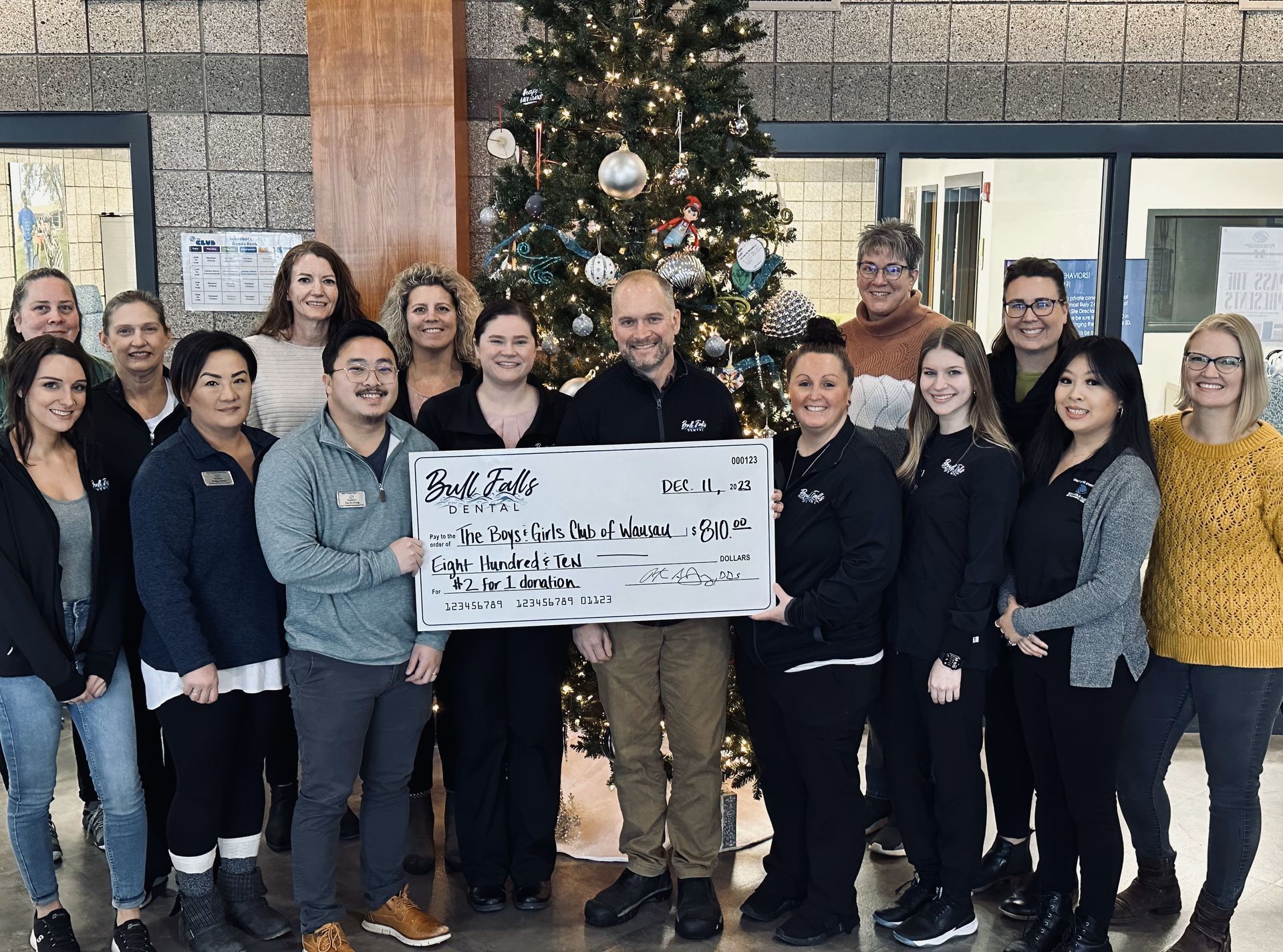 A group of people standing in front of a christmas tree holding a large check.