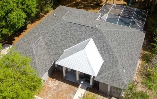Aerial view of a gray shingle roof with a white metal front section, next to a screened-in pool.