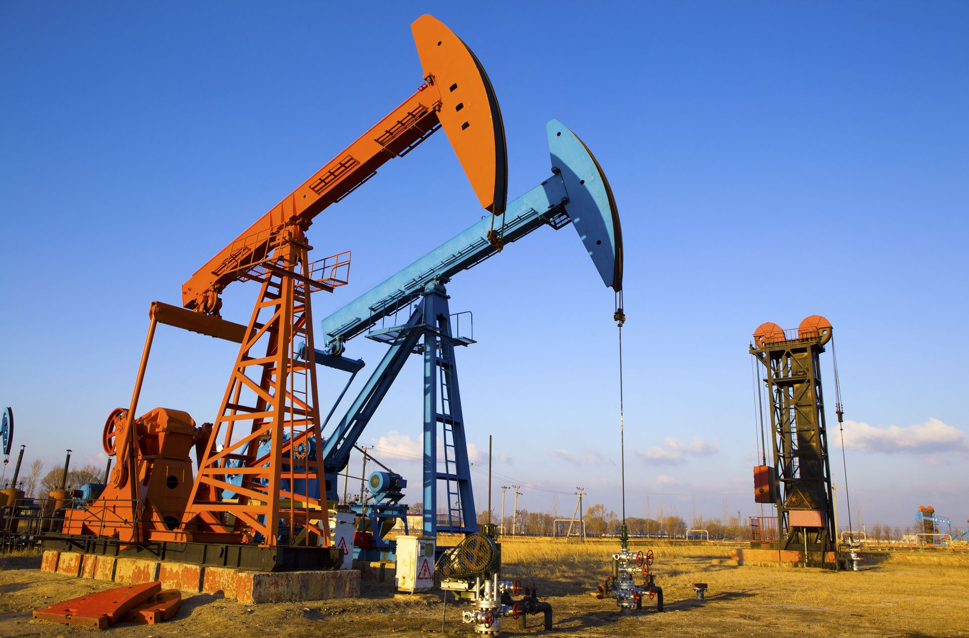 Two oil pumpjacks in a field, one orange and one blue, under a clear sky