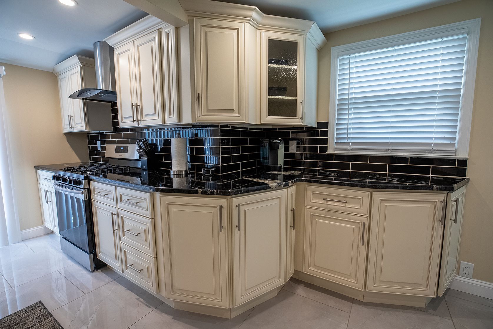 A kitchen with white cabinets , black counter tops , a stove , and a window.