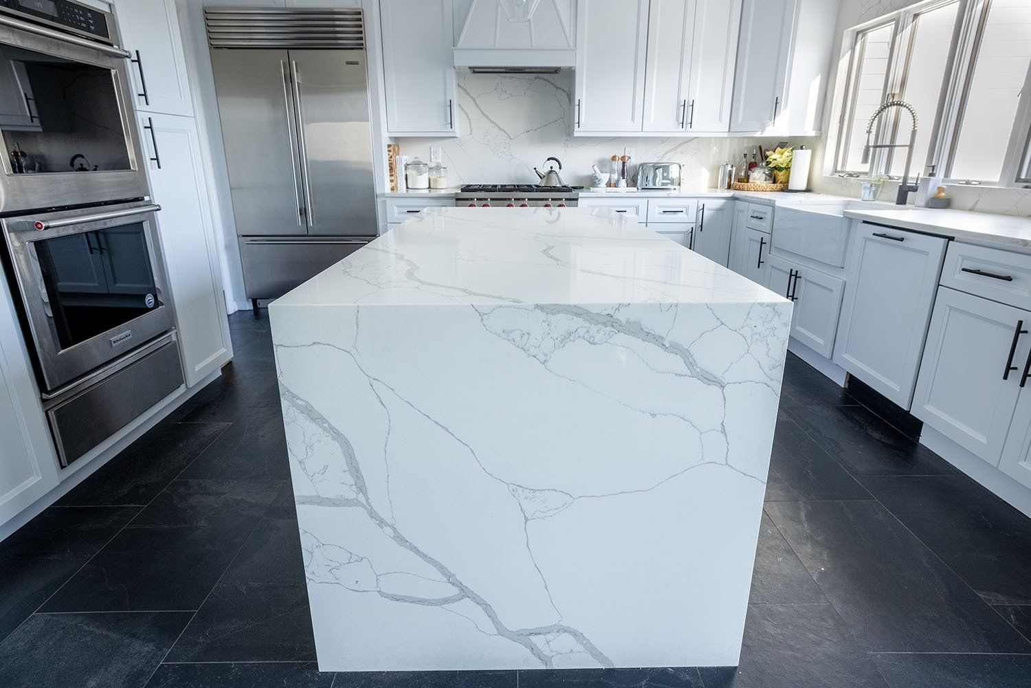 A kitchen with white cabinets and stainless steel appliances and a large white counter top.