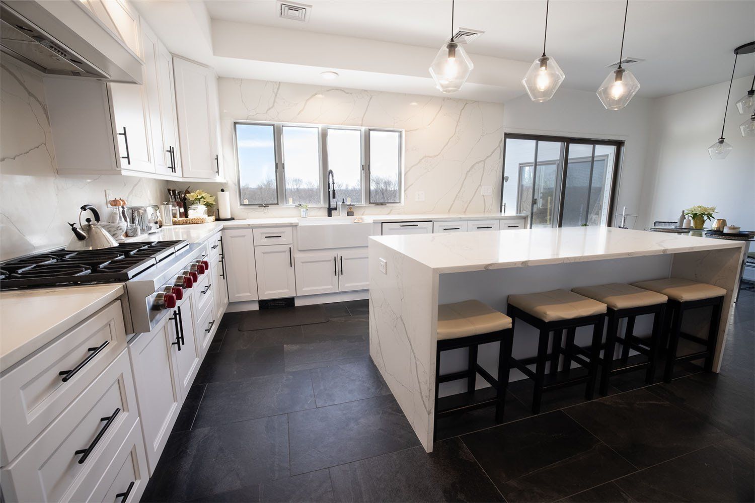 A kitchen with white cabinets , stools , a stove and a large island.