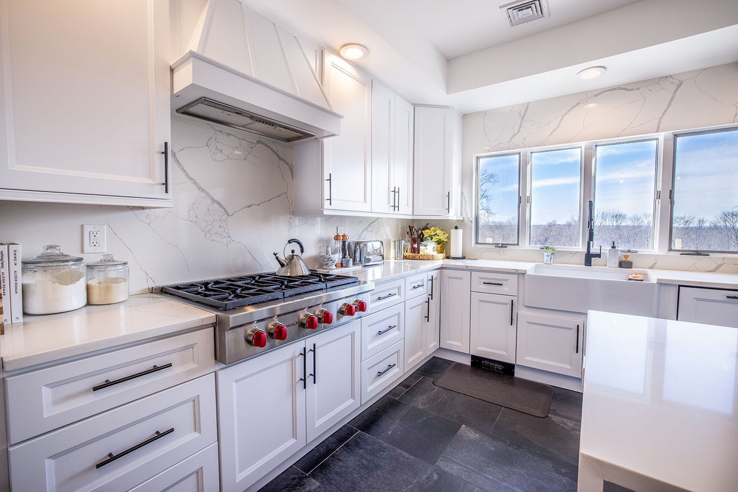 A kitchen with white cabinets , a stove , a sink , and a lot of windows.