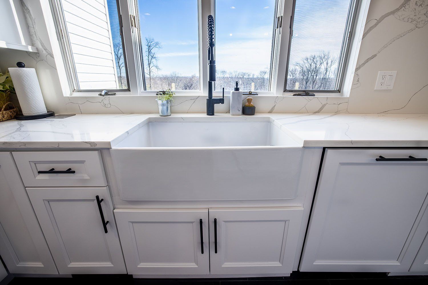 A kitchen sink with a window in the background and white cabinets.