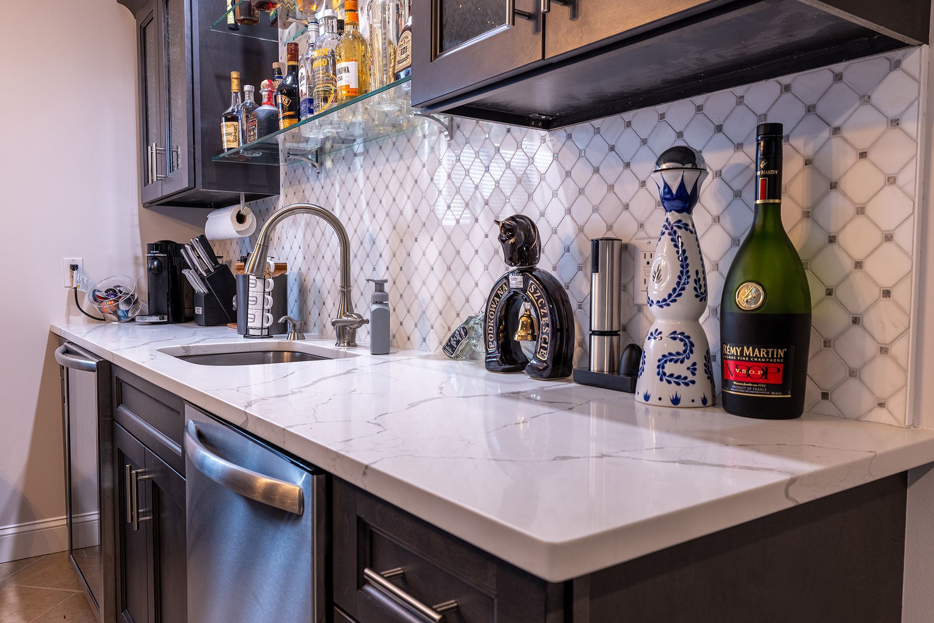 A kitchen with a sink , dishwasher , and bottles of alcohol on the counter.