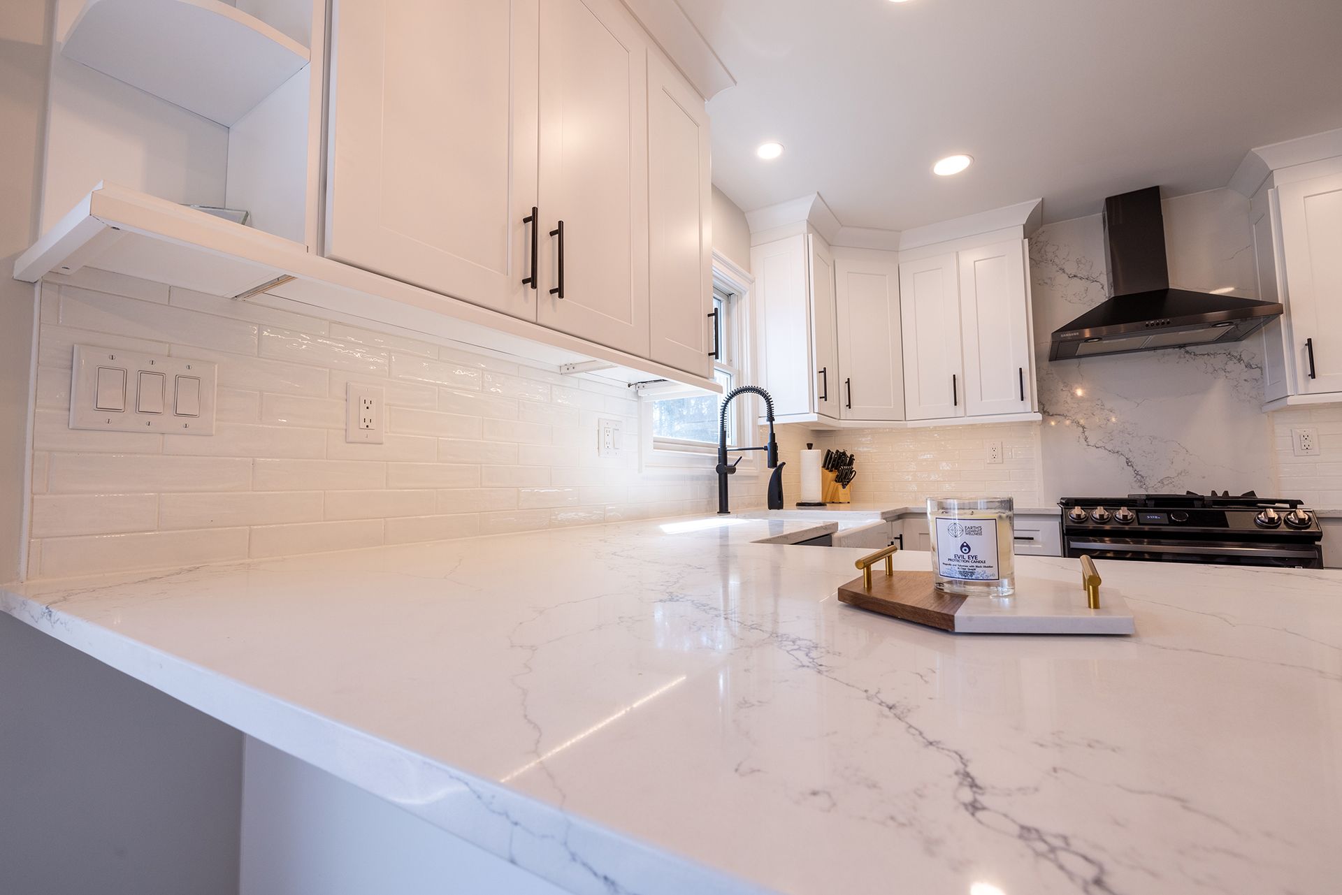 A kitchen with white cabinets , white counter tops , a stove and a sink.
