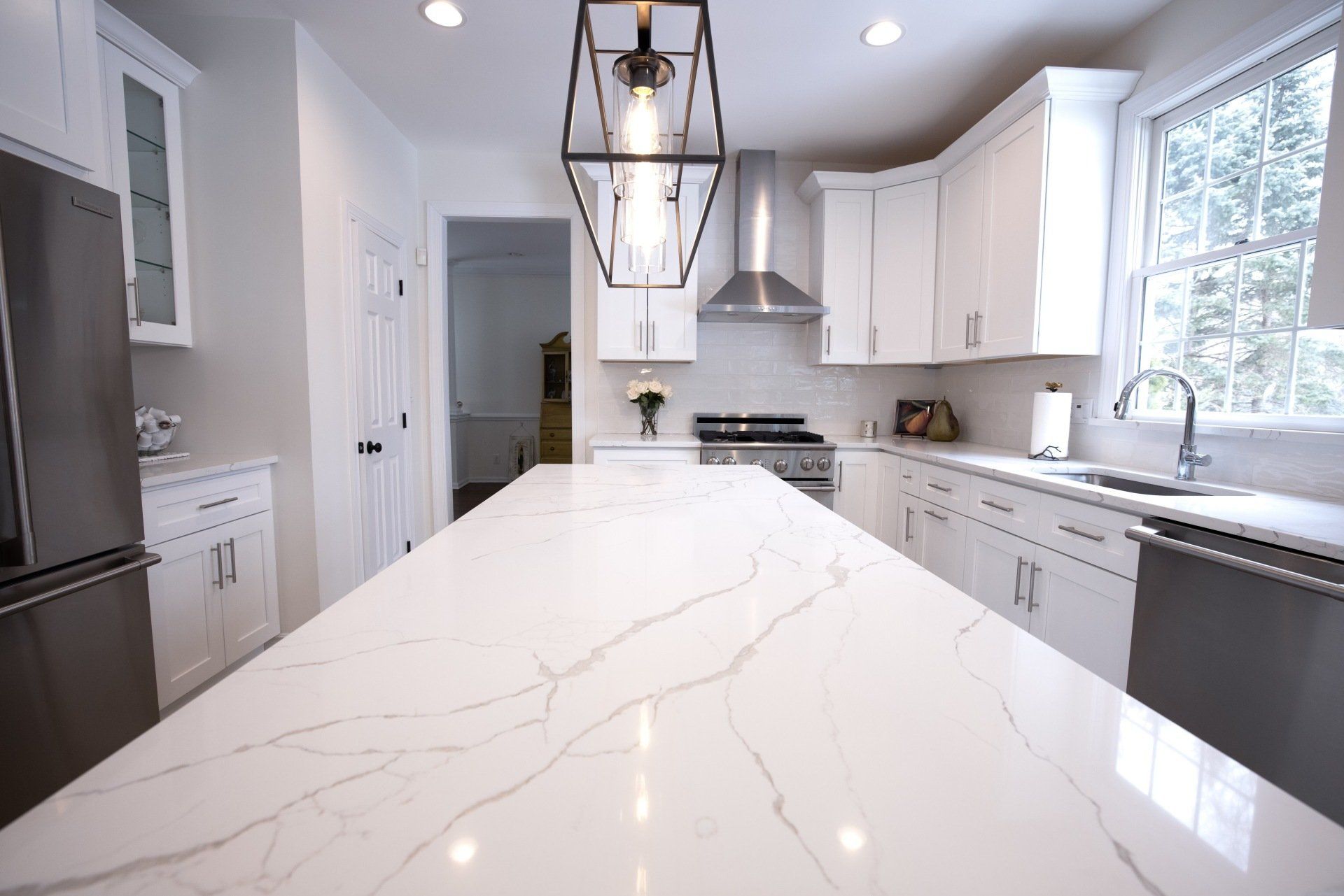 A kitchen with white cabinets , stainless steel appliances , and a large island.