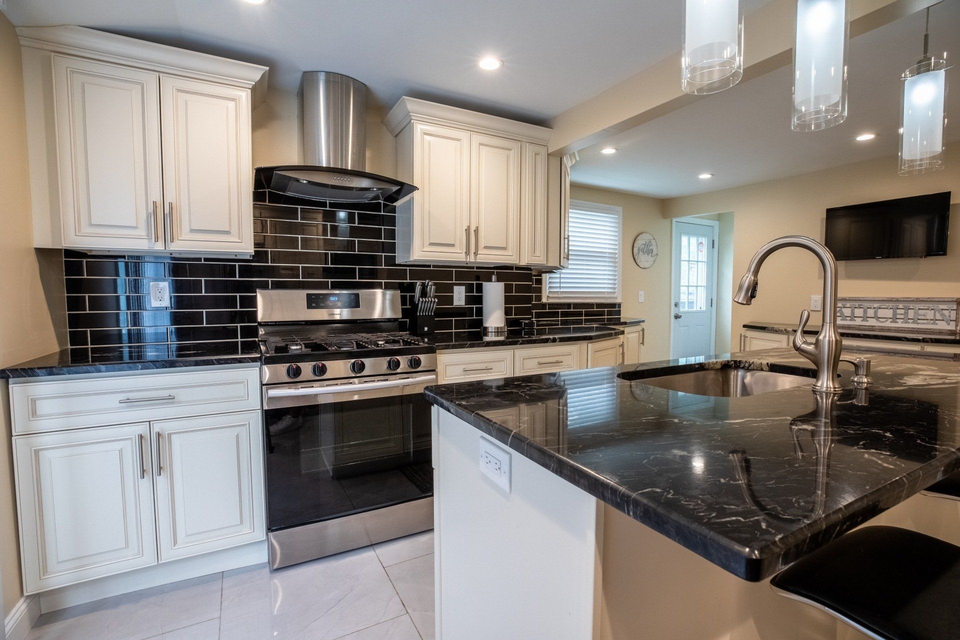 A kitchen with white cabinets , black counter tops , stainless steel appliances , and a sink.