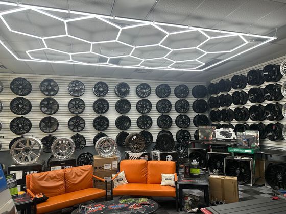 Tire shop interior with many wheels on display, orange couches, and hexagon-shaped ceiling lights.