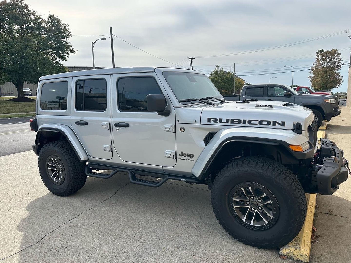 A silver Jeep Wrangler Rubicon is parked in a parking lot.