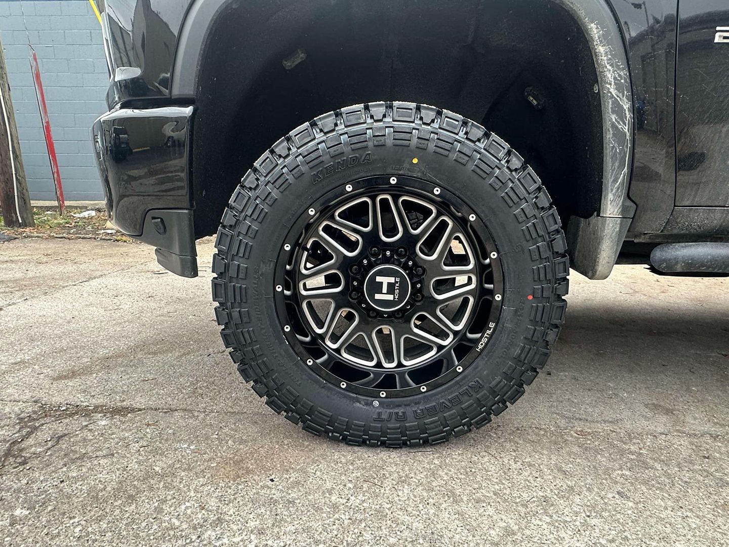 A black truck with black wheels and tires is parked on the side of the road.