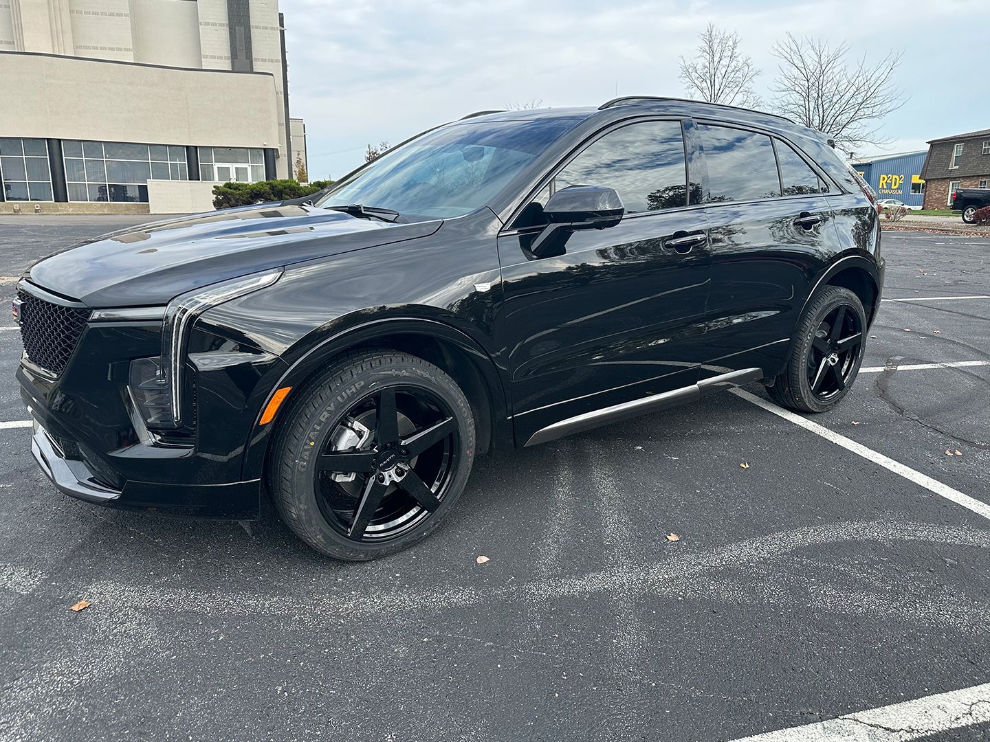 A black car is parked in a parking lot in front of a building.